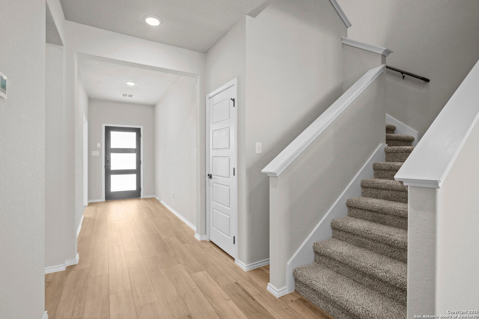 Bright entry hallway with oak floors, carpeted staircase, and modern front door in Davidson Homes The Sequoia A, Converse, Texas
