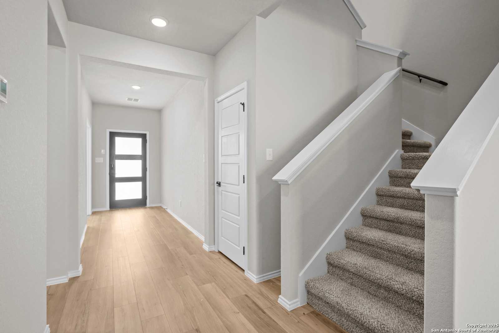 Bright entry hallway with oak floors, carpeted staircase, and modern front door in Davidson Homes The Sequoia A, Converse, Texas