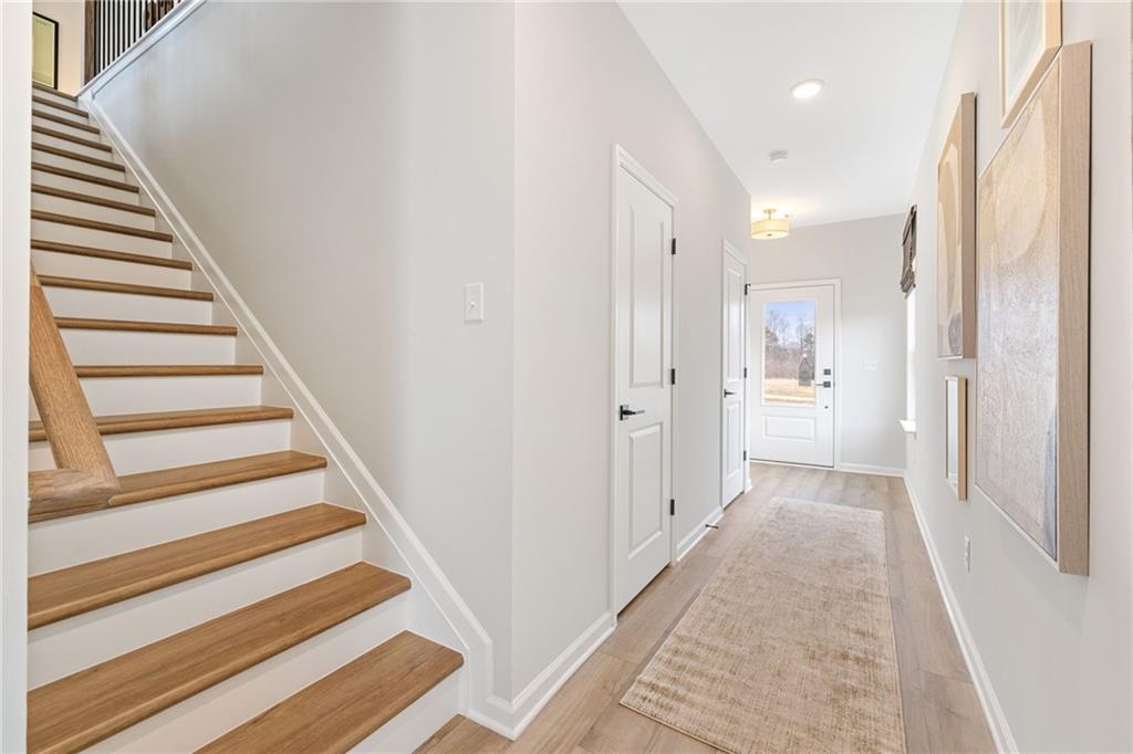 Bright foyer with oak staircase, light wood floors, beige runner rug, and glass front door in Davidson Homes Rabun B, Canton, GA