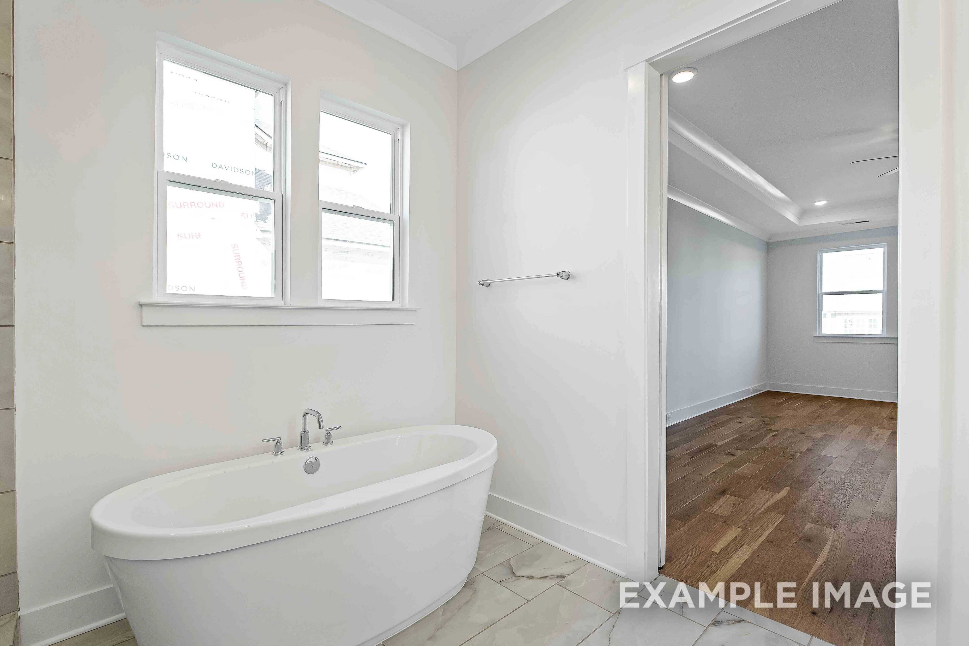 Spacious master bathroom in The Albany A with freestanding soaking tub, tiled floors, and hardwood bedroom view