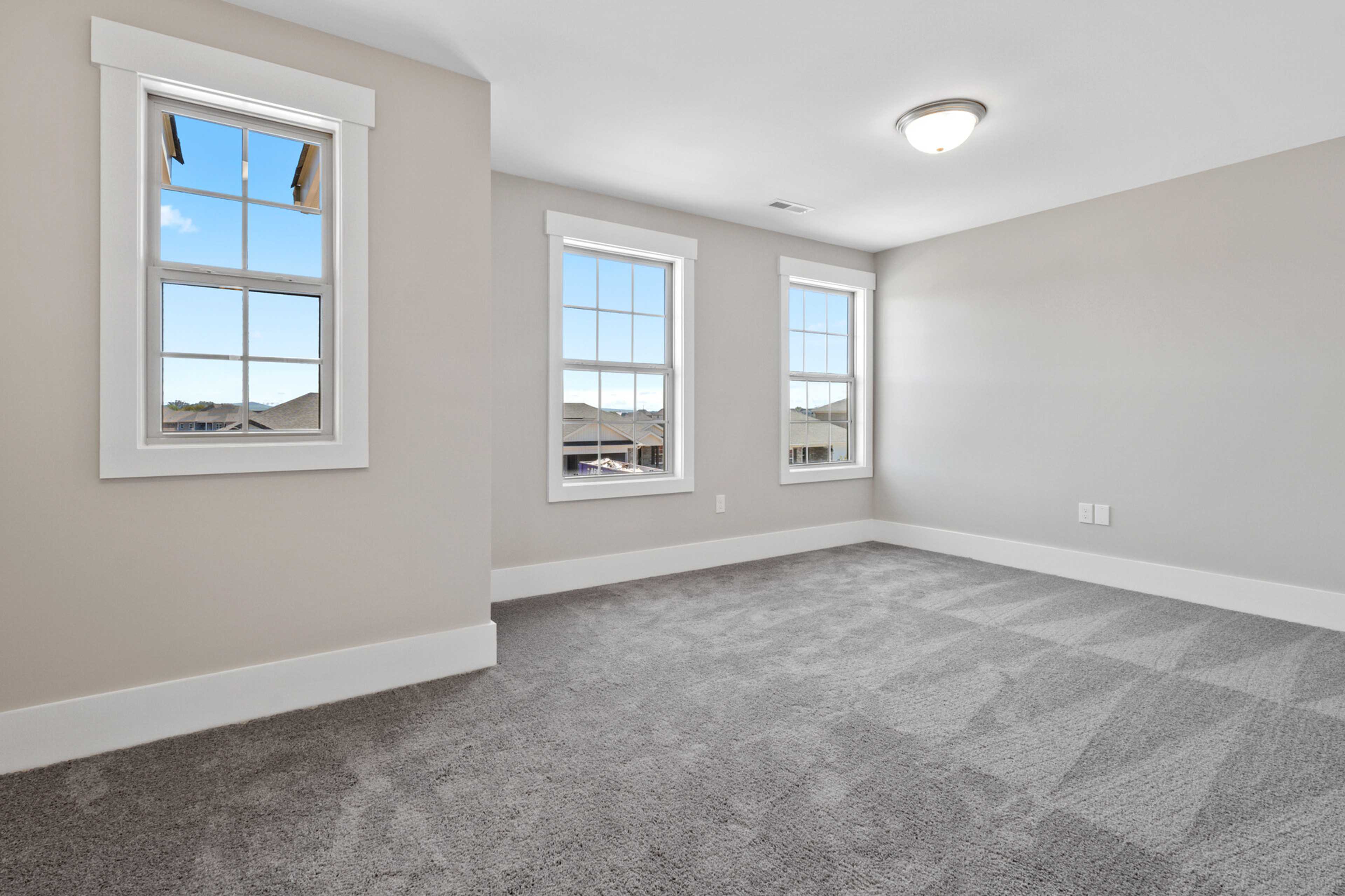 Spacious empty bedroom with gray walls, carpet flooring, and large windows overlooking neighborhood at Little Burwell Estates in Harvest Alabama