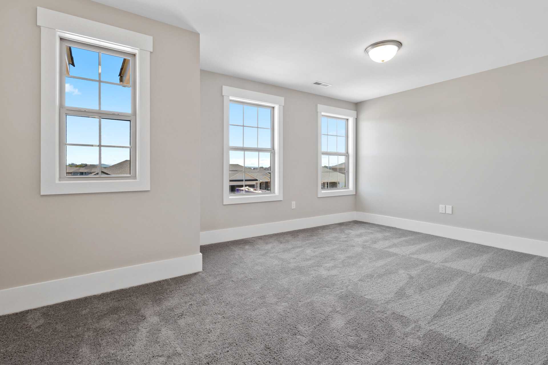 Spacious empty bedroom with gray walls, carpet flooring, and large windows overlooking neighborhood at Little Burwell Estates in Harvest Alabama