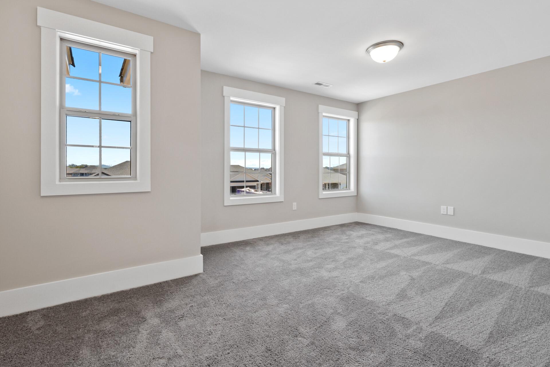 Spacious empty bedroom with gray walls, carpet flooring, and large windows overlooking neighborhood at Little Burwell Estates in Harvest Alabama