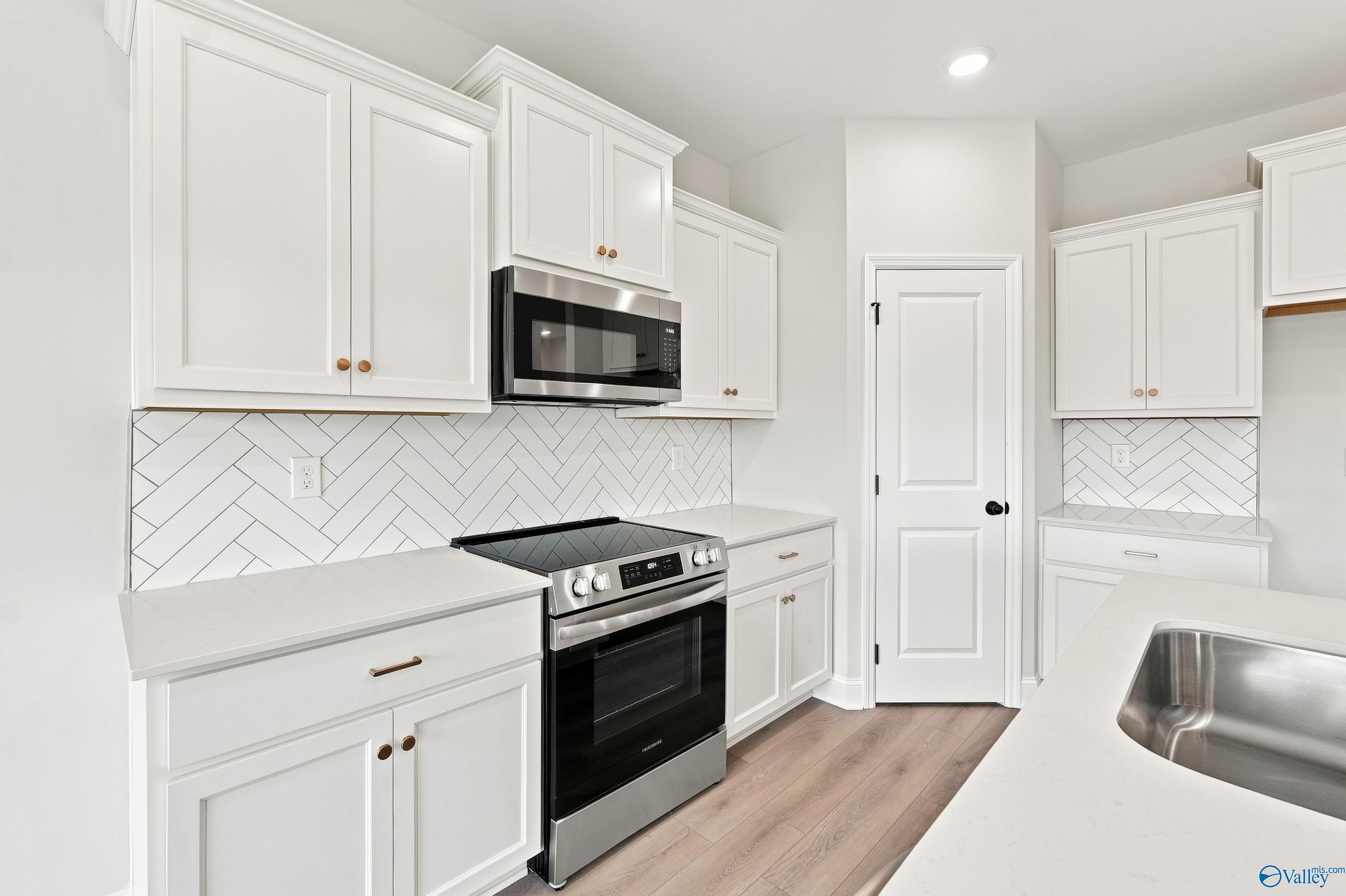 Modern kitchen with white cabinets, herringbone backsplash, and stainless appliances in The Asheville E, Forest Glen, AL.