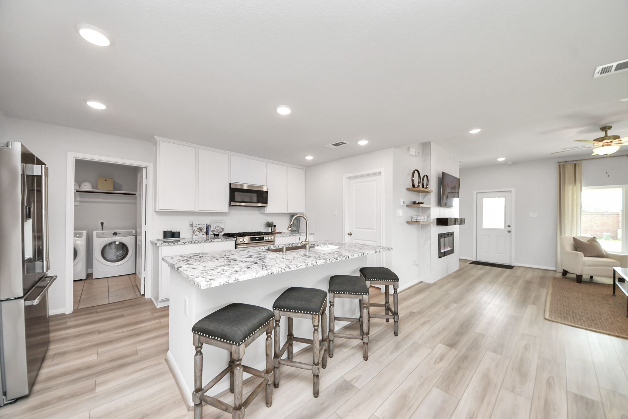 Modern kitchen with granite island and white cabinets at Sunterra in Katy, TX, featuring an adjacent laundry room.
