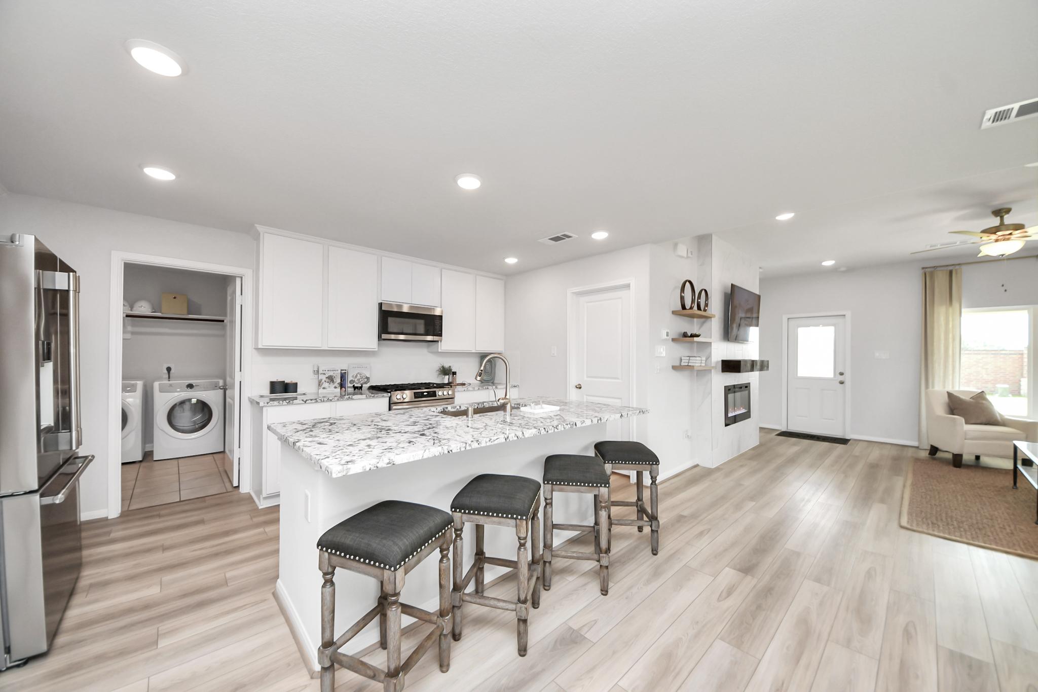 Modern kitchen with granite island and white cabinets at Sunterra in Katy, TX, featuring an adjacent laundry room.