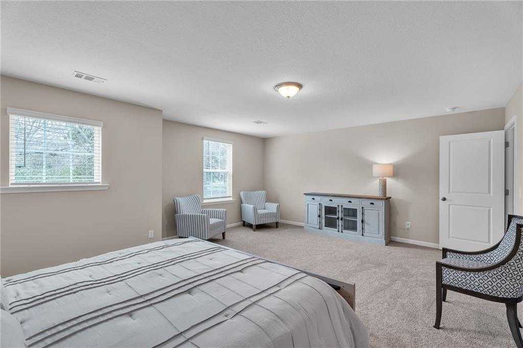 Spacious secondary bedroom with queen bed, blue armchairs, and beige walls in Davidson Homes The Bartlett, Phenix City, Alabama