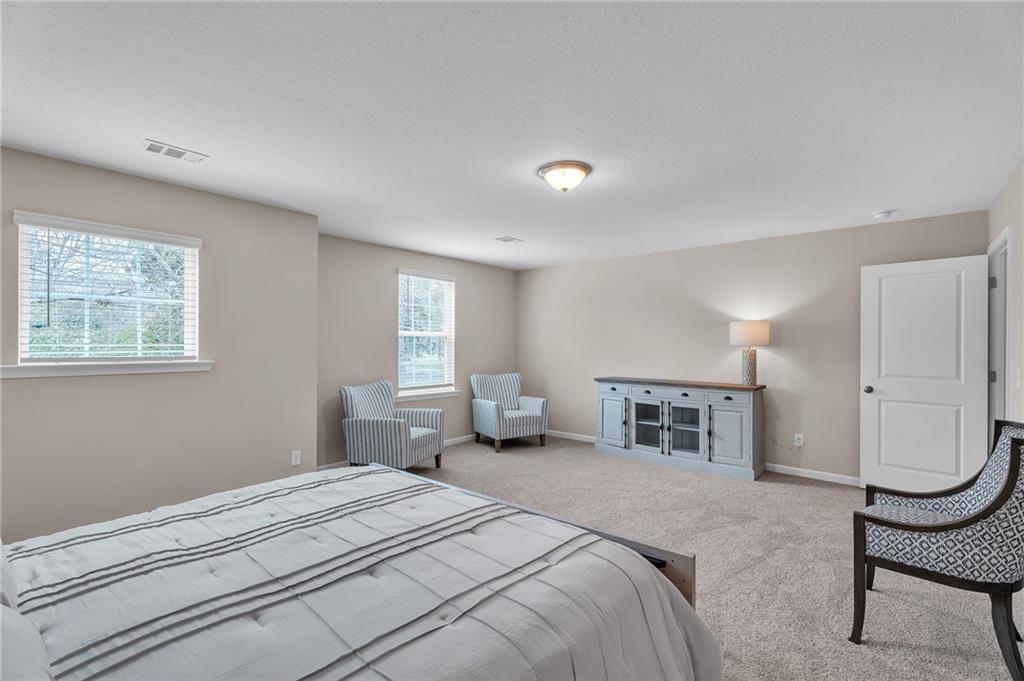 Spacious secondary bedroom with queen bed, blue armchairs, and beige walls in Davidson Homes The Bartlett, Phenix City, Alabama