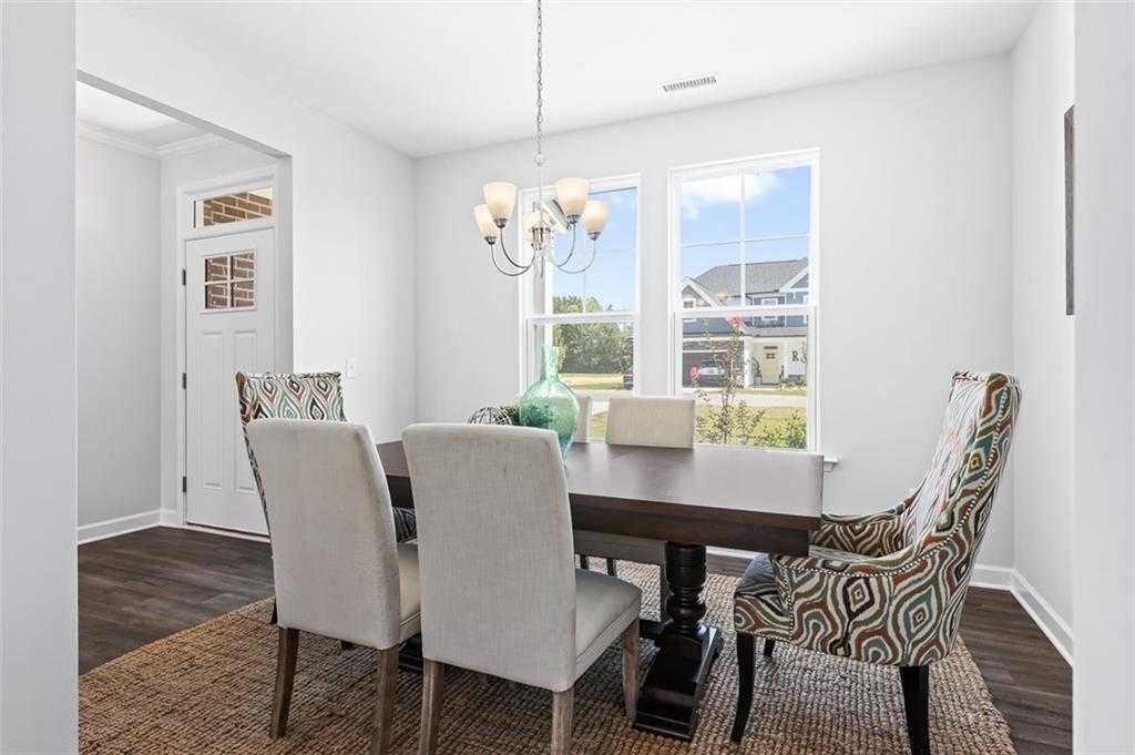 Elegant dining room with wooden table, patterned armchairs, chandelier, large windows in Davidson Homes The Willow E, Wehunt Meadows, Hoschton
