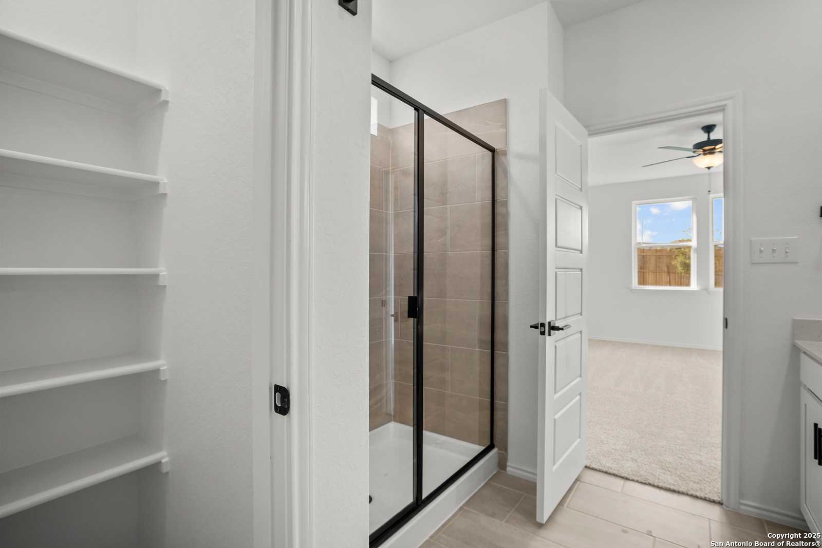 Modern master bathroom with frameless glass shower, linen shelving, and bedroom access in Davidson Homes The Daphne K, San Antonio