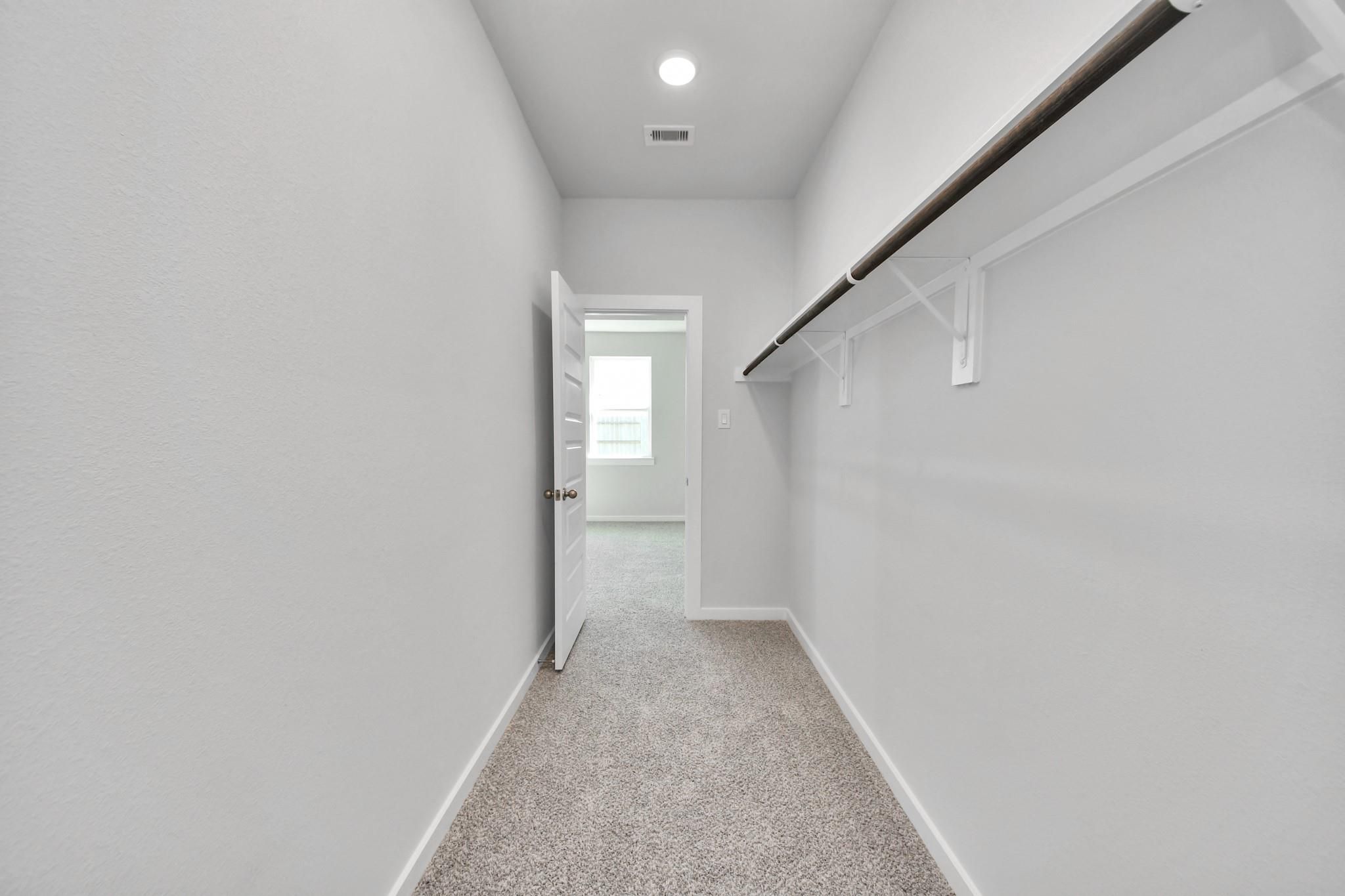 Walk-in closet with shelving and carpet in The Colorado G floor plan by Davidson Homes in Emberly, Beasley, Texas.