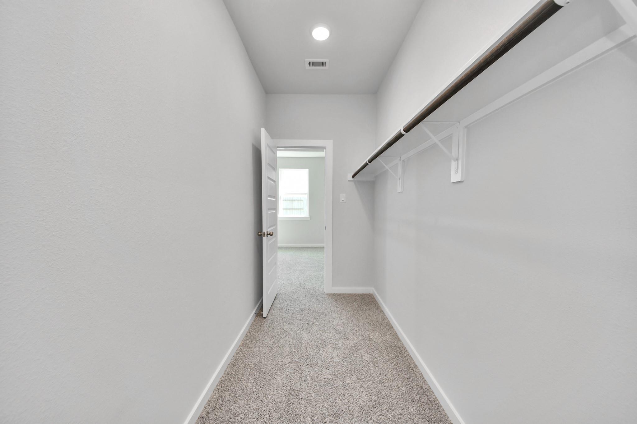 Walk-in closet with shelving and carpet in The Colorado G floor plan by Davidson Homes in Emberly, Beasley, Texas.