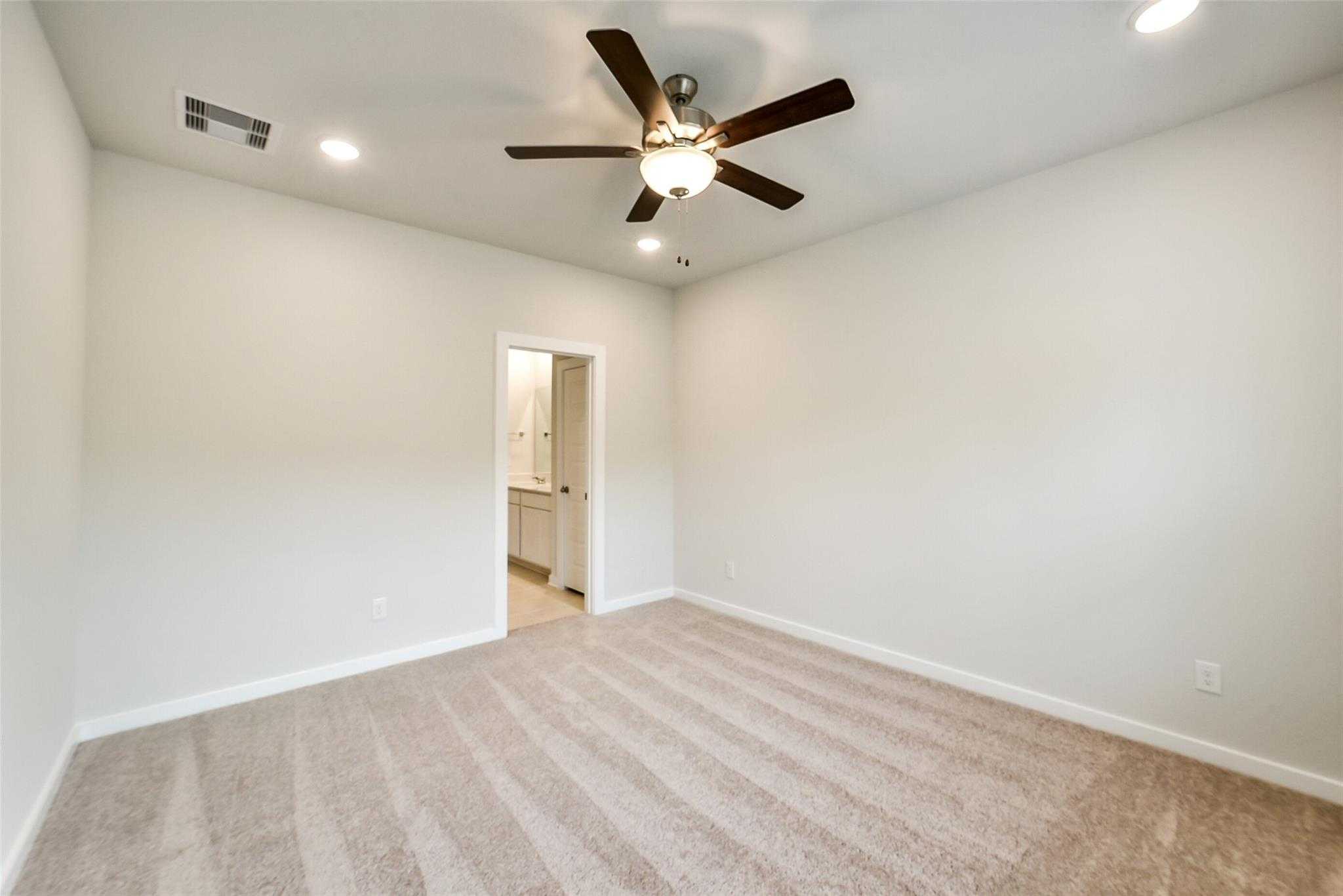 Spacious secondary bedroom with ceiling fan, beige carpet, and en-suite bath door in Davidson Homes The Blanco E, Magnolia, Texas