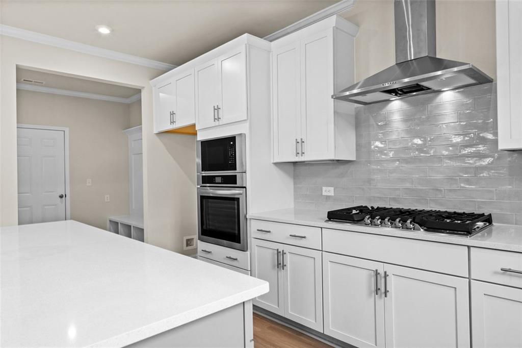 Modern white kitchen island with stainless steel cooktop, double oven, subway tile backsplash in Davidson Homes The Hickory B, Hoschton, GA