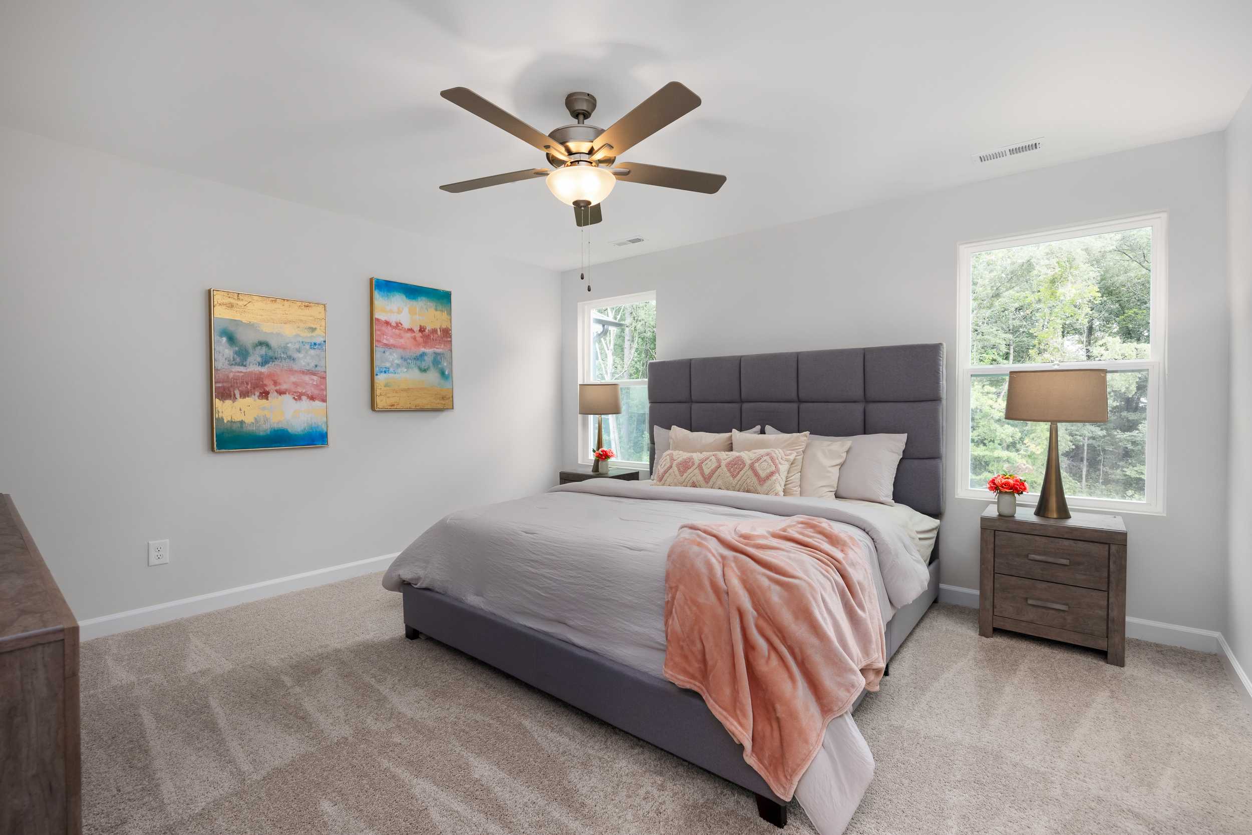 Spacious bedroom at Gregory Village Townhomes in Lillington NC with king bed, neutral tones, abstract wall art, and ceiling fan