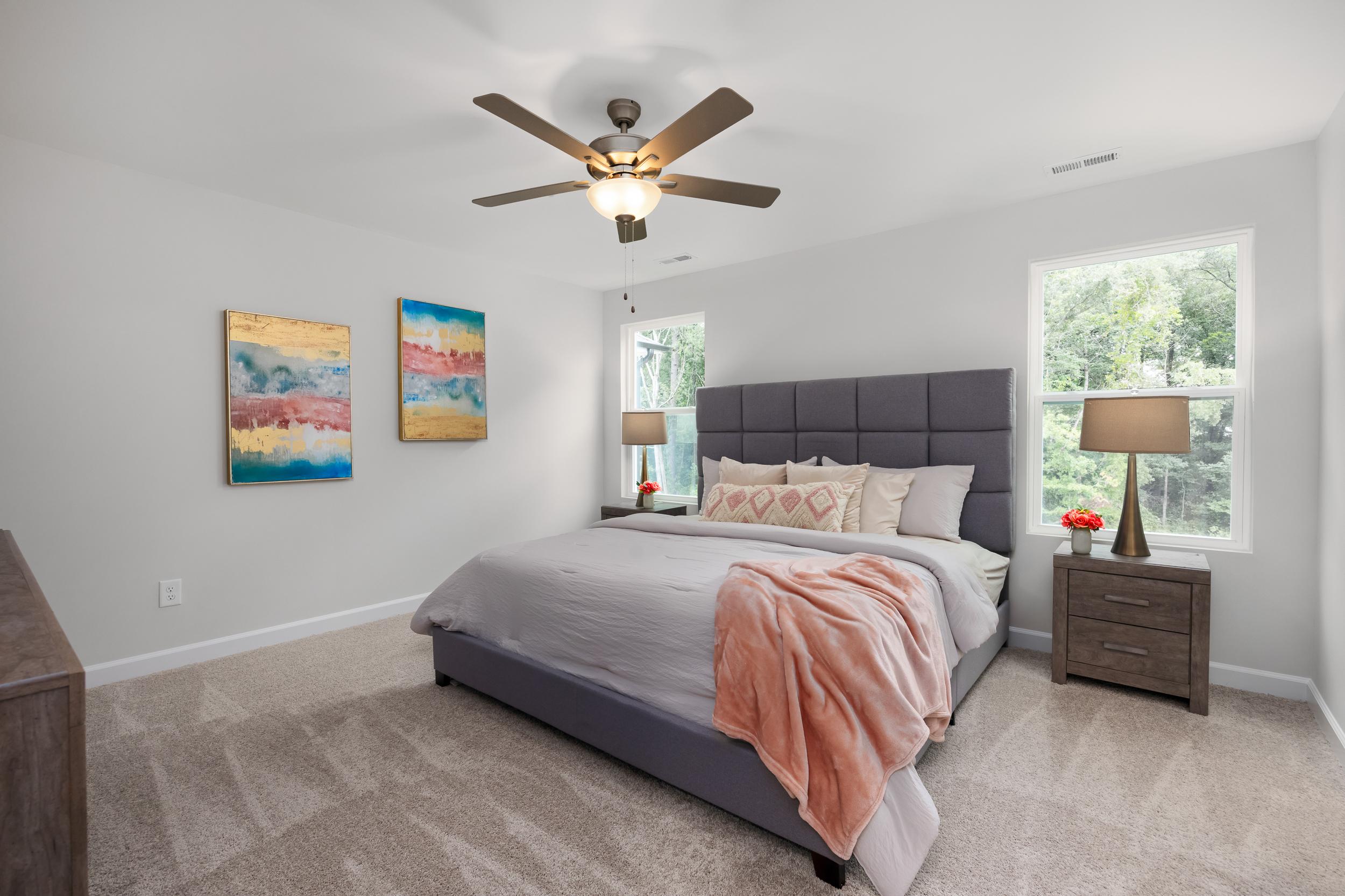 Spacious bedroom at Gregory Village Townhomes in Lillington NC with king bed, neutral tones, abstract wall art, and ceiling fan