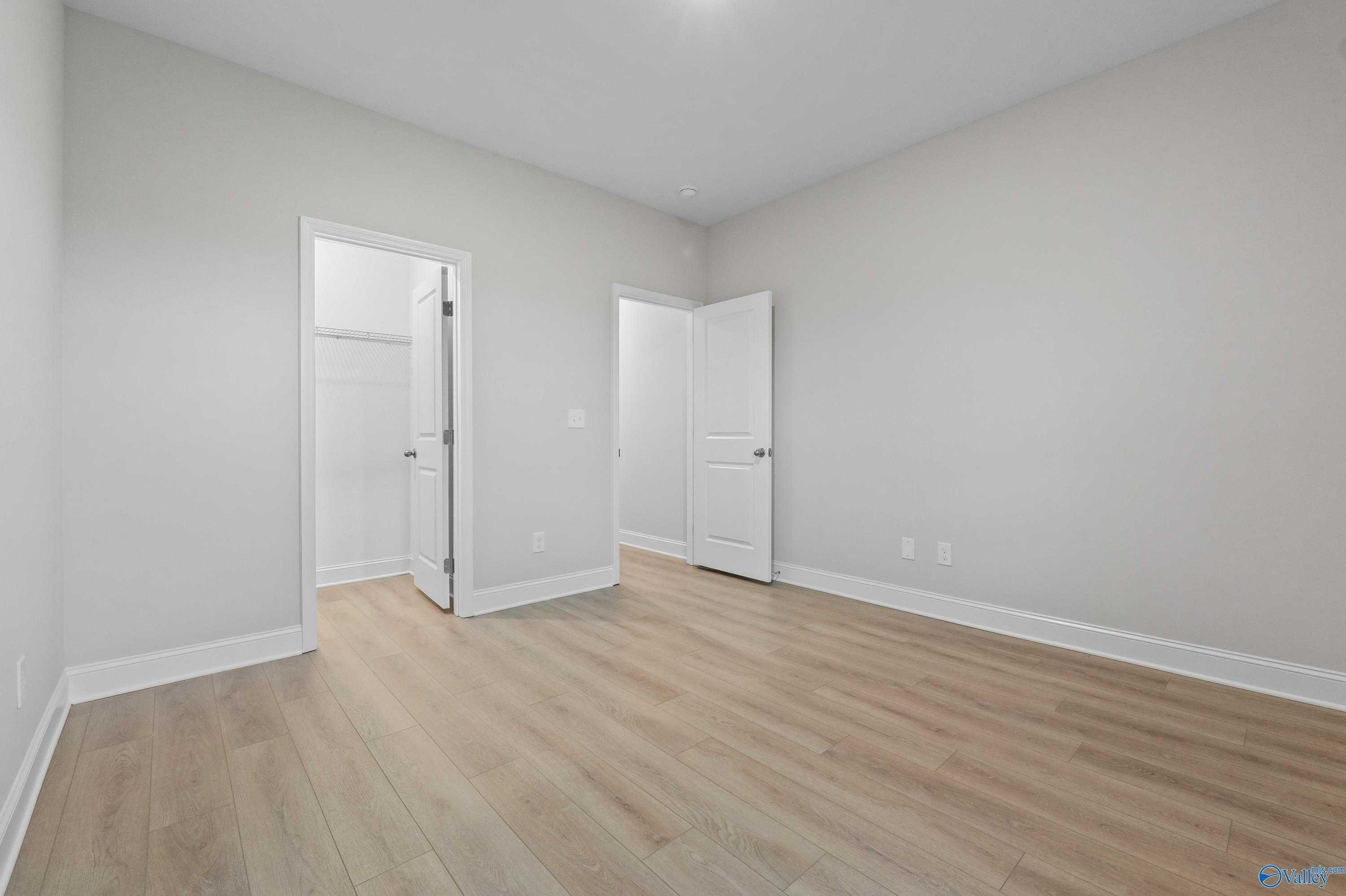 Bright bedroom hallway with light gray walls, hardwood floors, and open doors to bath and closet in The Lanier home, Harvest, AL