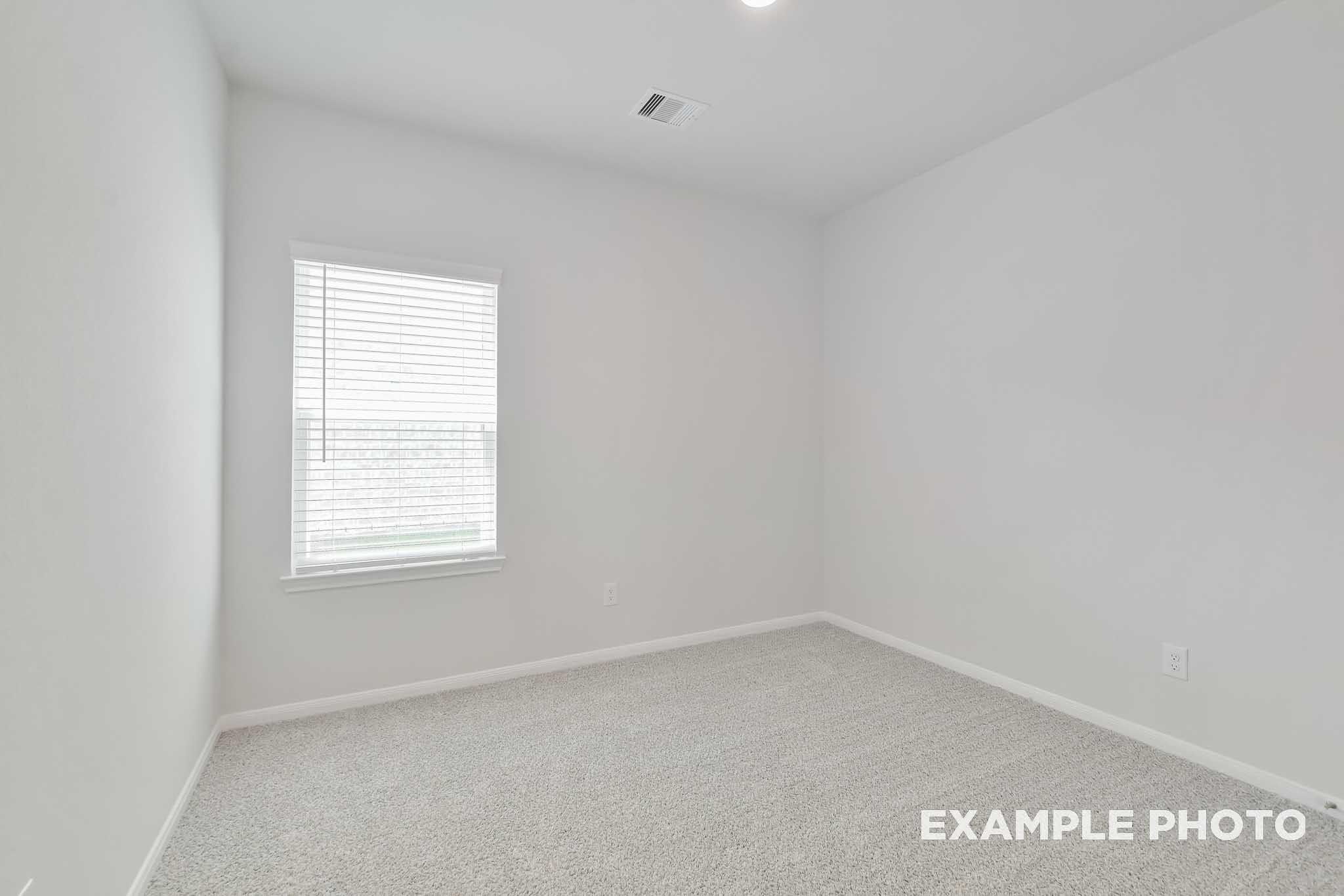 Bright empty secondary bedroom with white walls, blinds-covered window, and carpet in Davidson Homes The Frio F, Conroe TX