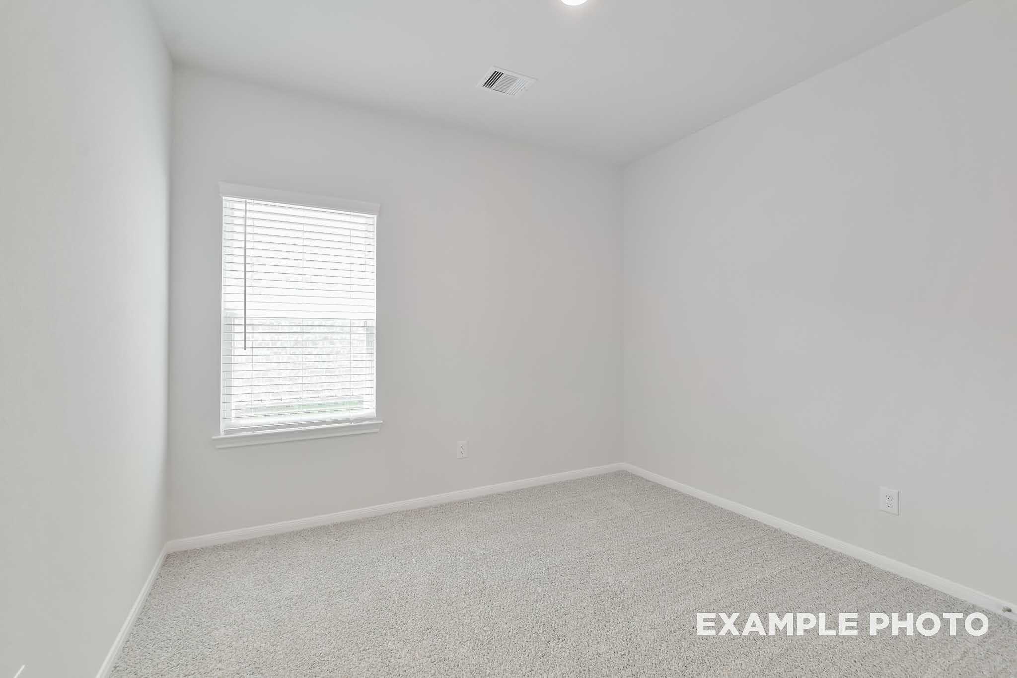 Bright empty secondary bedroom with white walls, blinds-covered window, and carpet in Davidson Homes The Frio F, Conroe TX