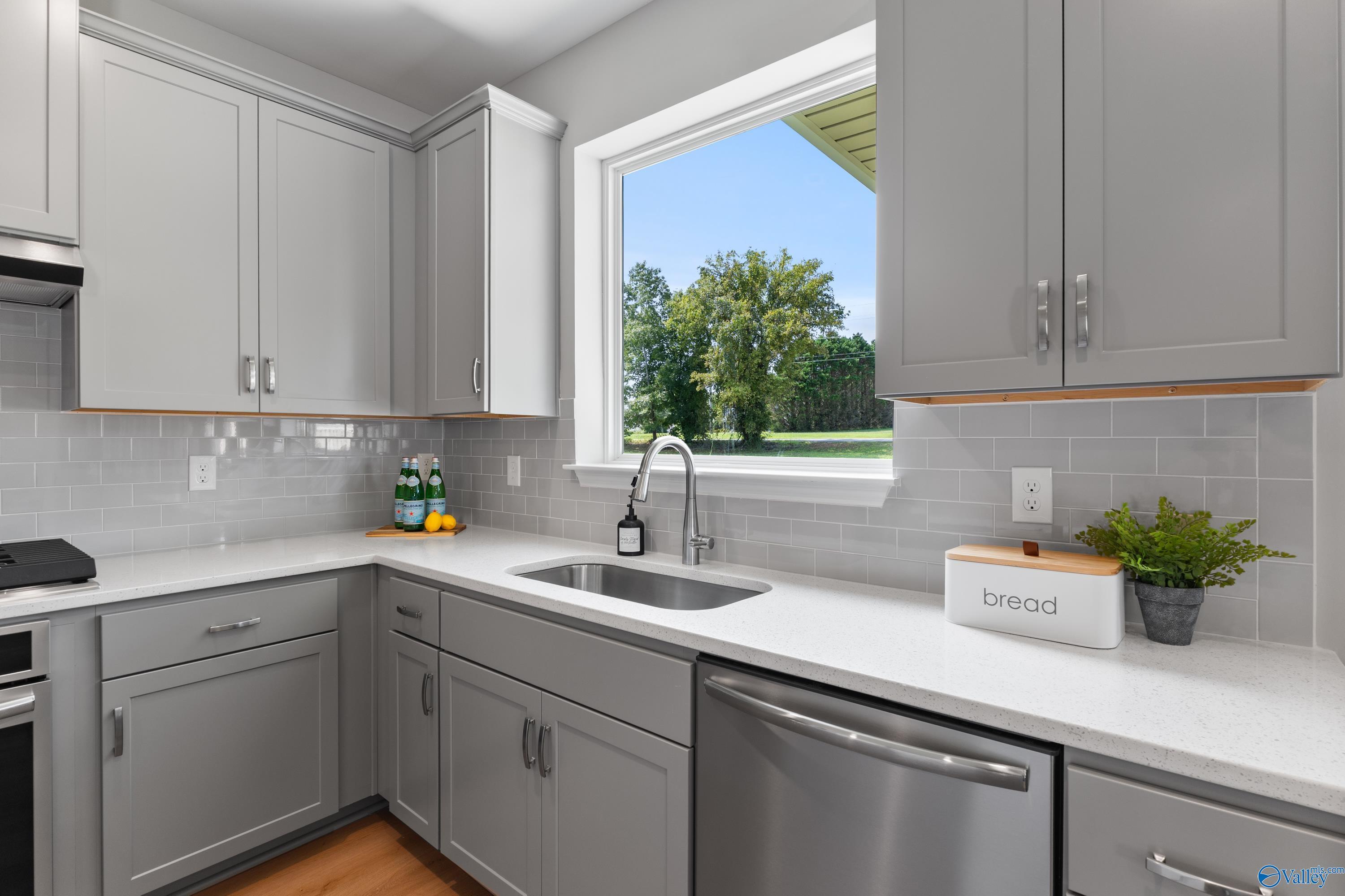 Modern gray shaker kitchen with white quartz counters, stainless sink, and tree-view window in Davidson Homes The Charm, Huntsville AL