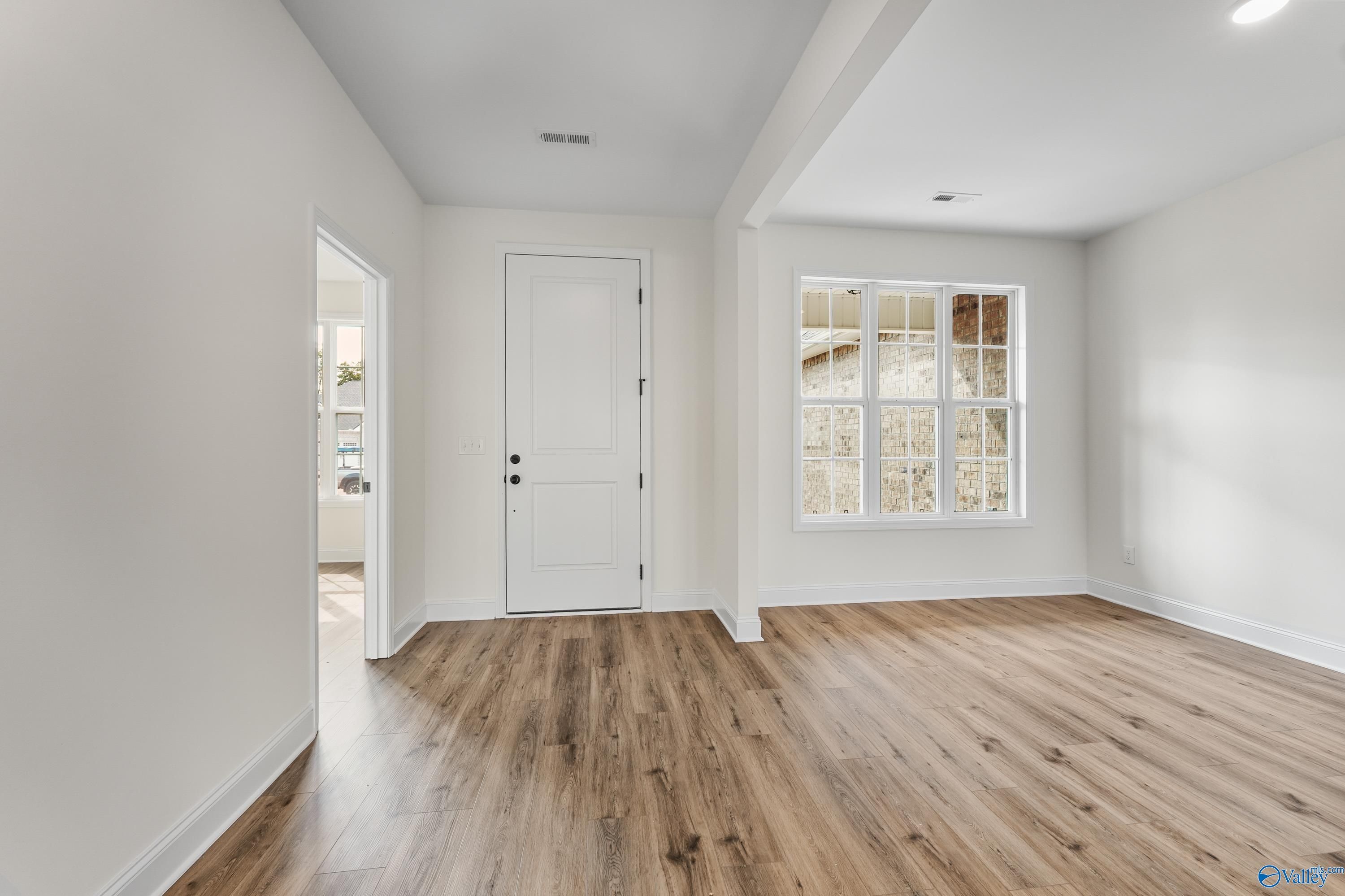 Bright hallway with hardwood floors, white doors, and large grid windows overlooking greenery in Davidson Homes The Finleigh, Harvest, Alabama
