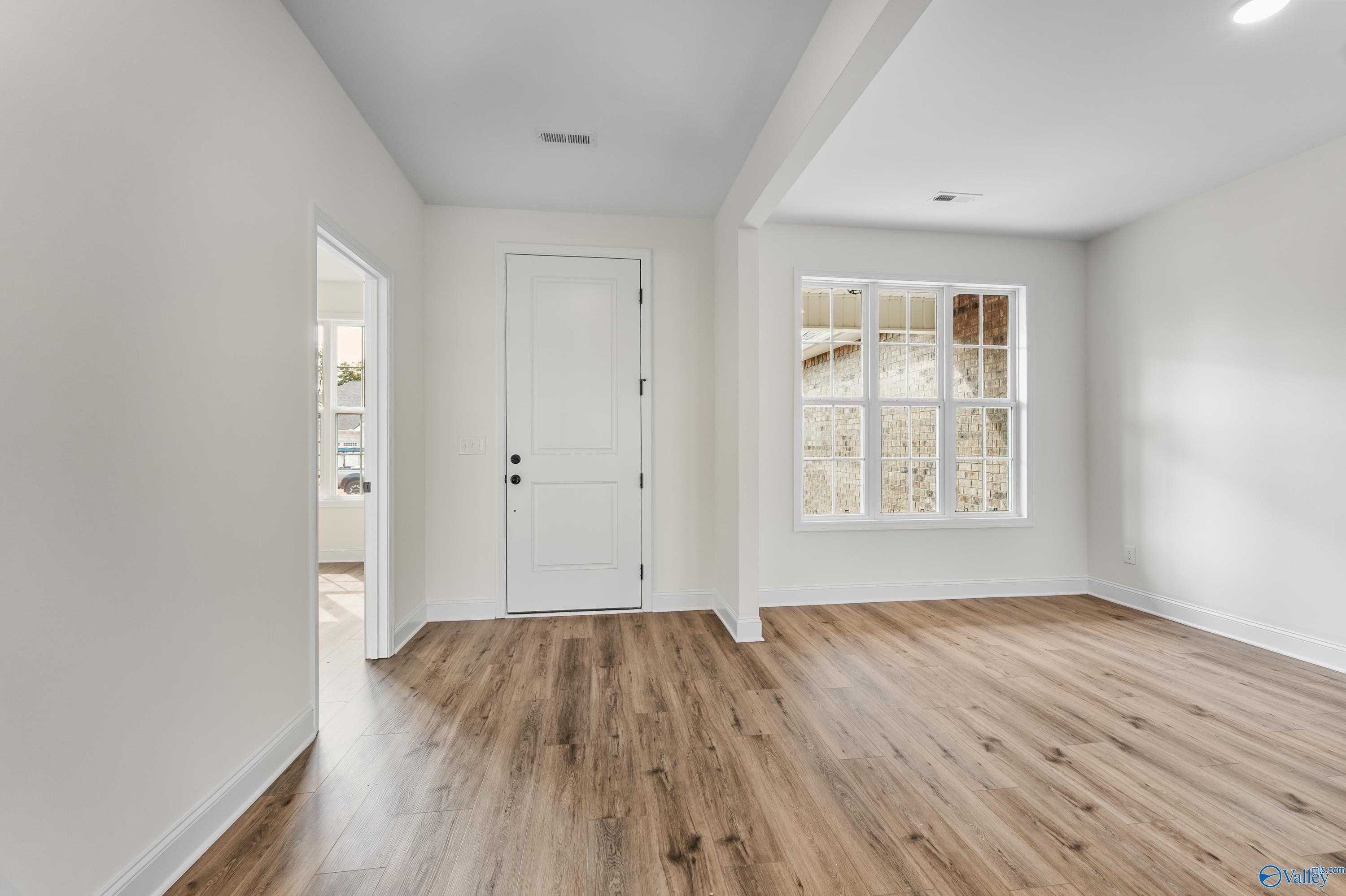 Bright hallway with hardwood floors, white doors, and large grid windows overlooking greenery in Davidson Homes The Finleigh, Harvest, Alabama
