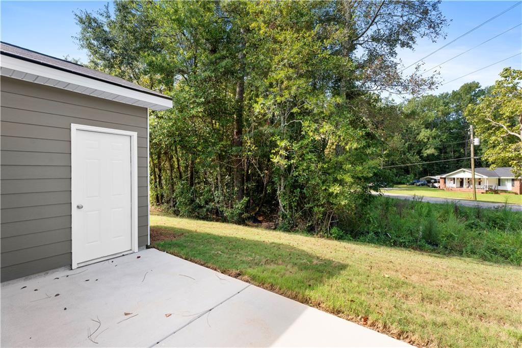 Detached gray garage with white door on concrete pad amid lush trees and grassy slope in Summer Vineyard 3-bedroom home, Phenix City, Alabama