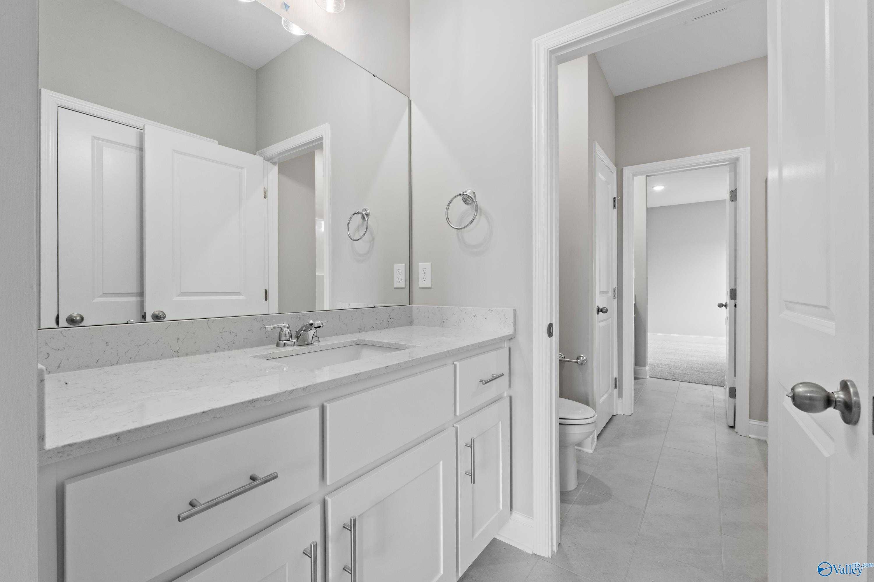 Modern guest bathroom with quartz vanity, large mirror, and tile flooring in Davidson Homes The Finleigh, Meridianville, Alabama