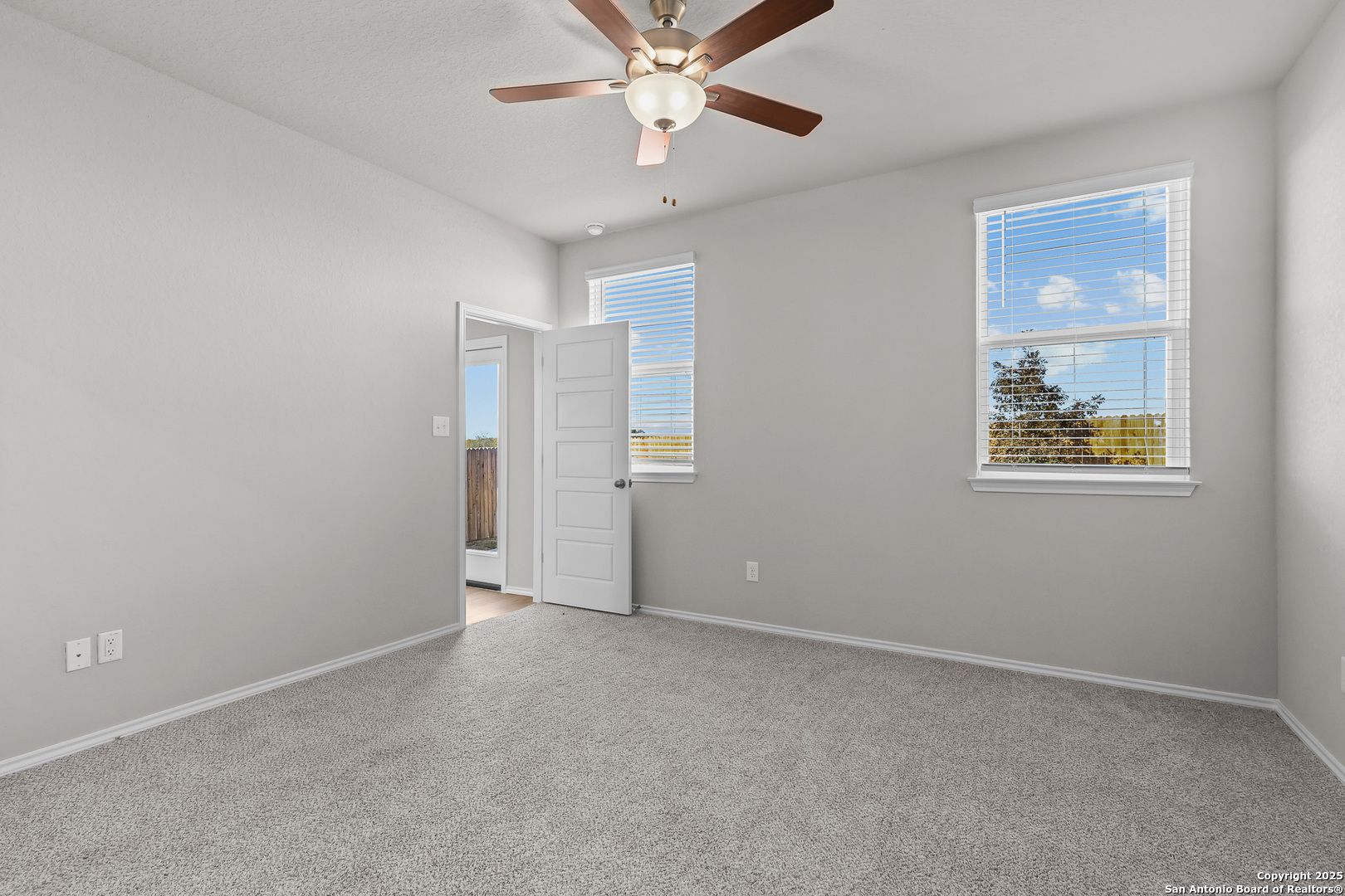 Bright bedroom with ceiling fan, gray carpet, light walls, and tree-view windows in Davidson Homes The Colorado B, San Antonio