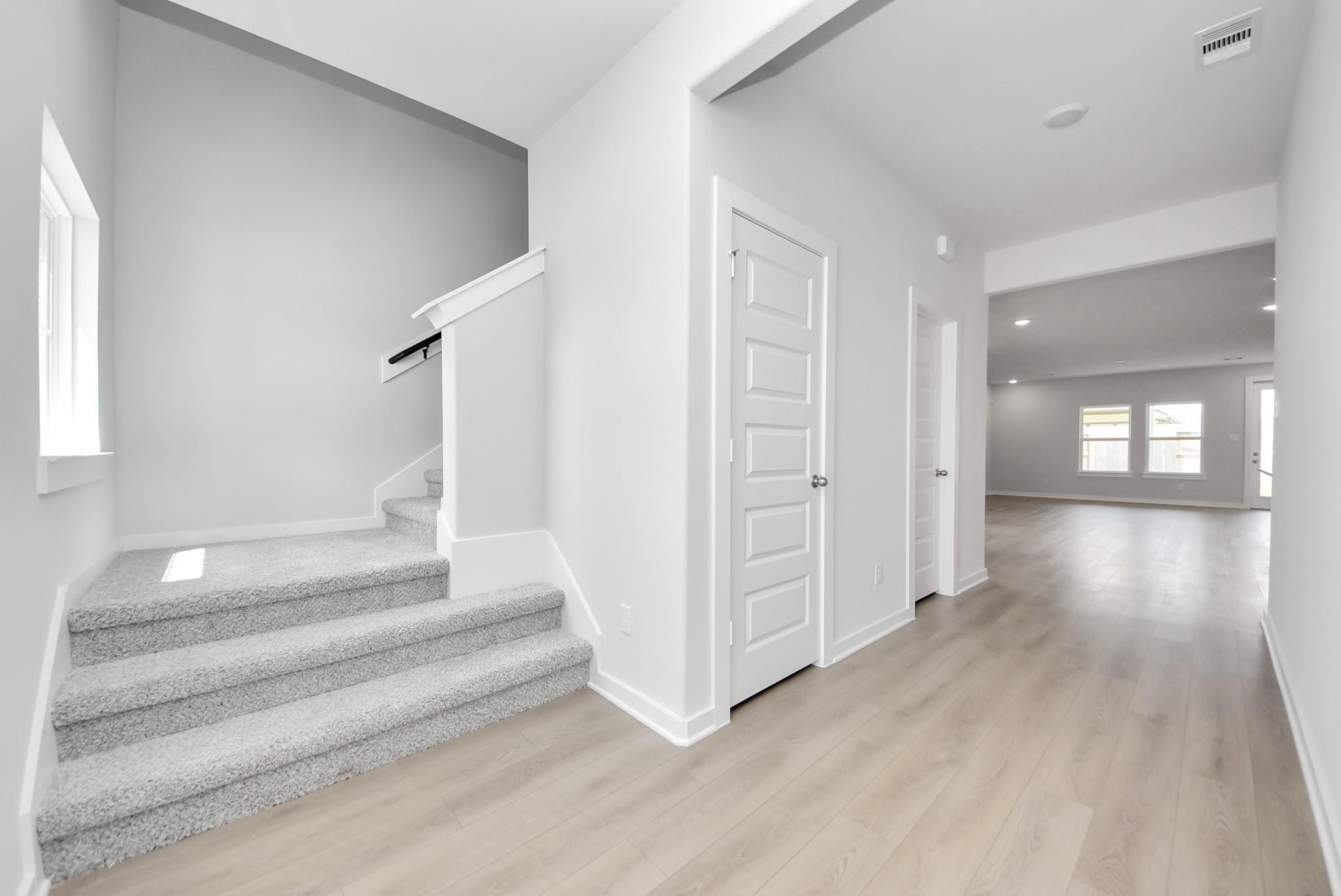 Bright, open entryway with carpeted stairs and wood-look flooring in The Verano B floor plan at Sunterra, Katy, Texas.