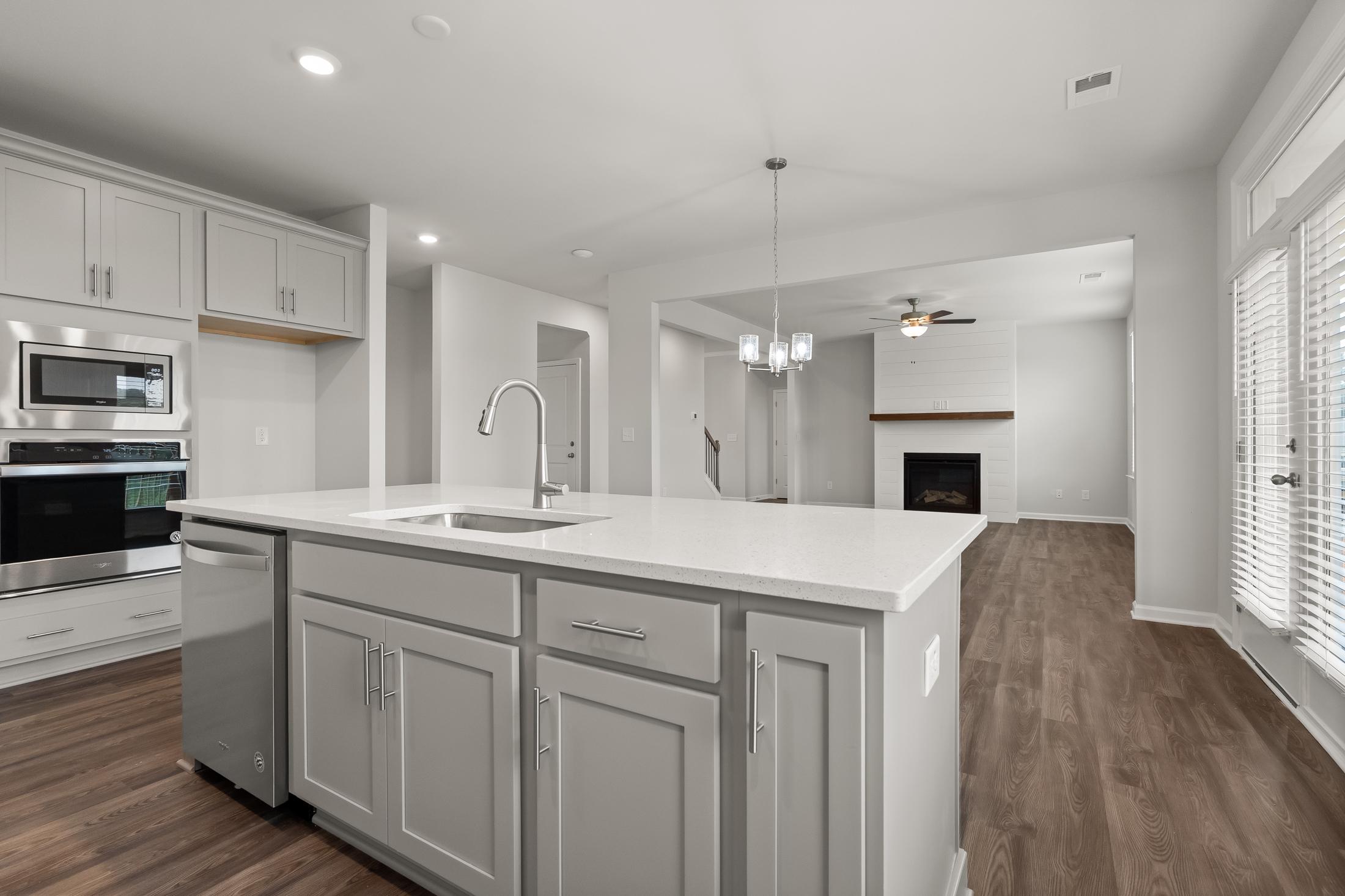 Spacious open-concept kitchen at Reverie at East Lake in McDonough GA with white island, stainless appliances, and adjacent living area featuring fireplace