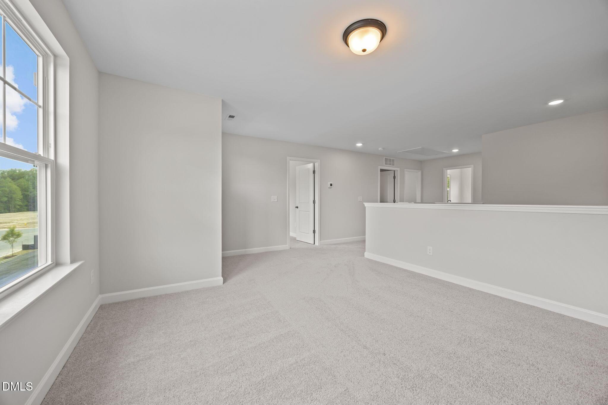Spacious upstairs hallway with gray carpet, neutral walls, large windows, and balcony railing in The Willow D floor plan, Wendell, NC