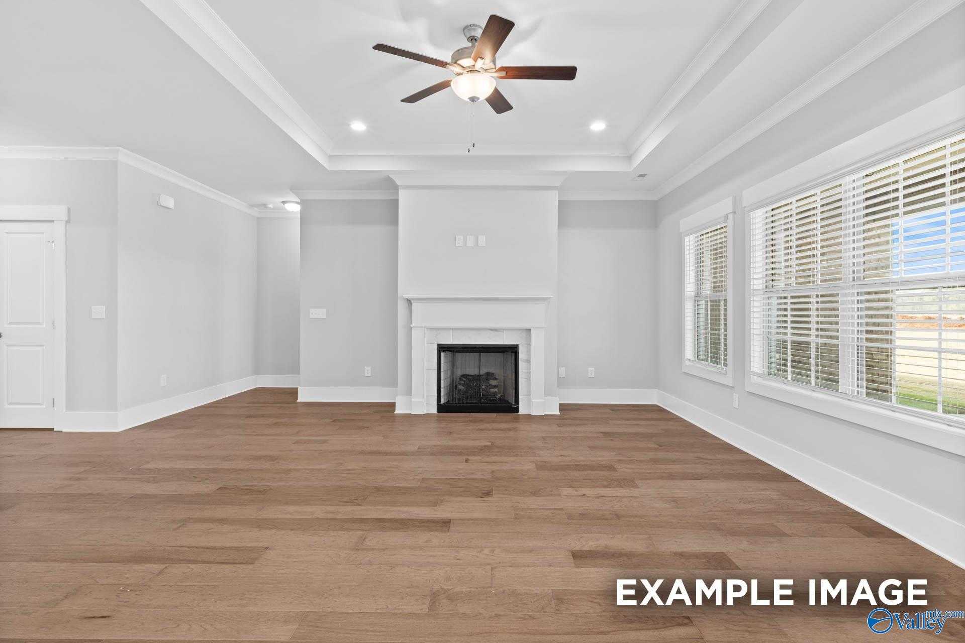 Bright living room with gas fireplace, ceiling fan, large windows, blinds, and hardwood floors in Davidson Homes The Rockford, Meridianville, AL