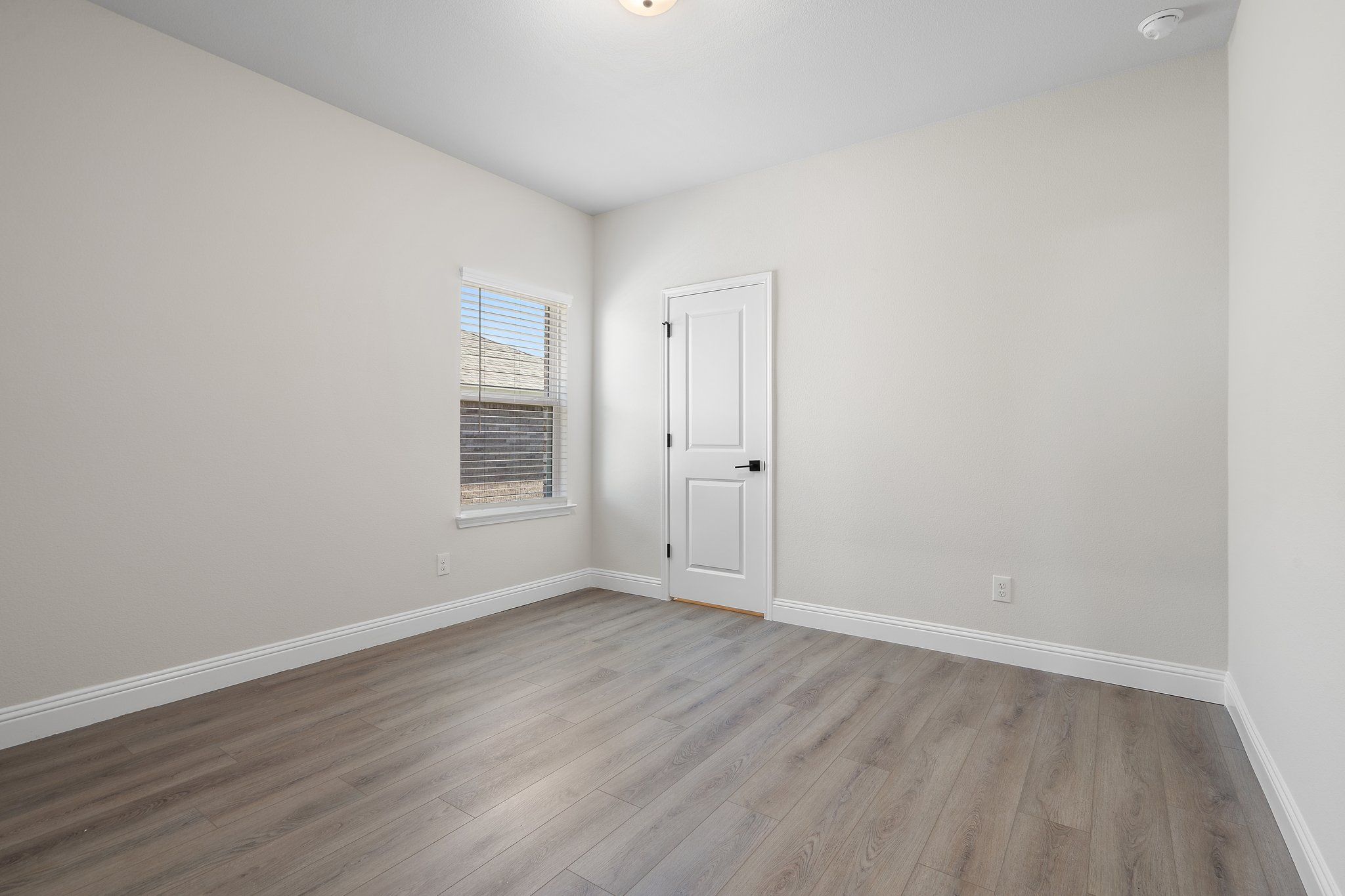 Bright, neutral-toned bedroom in The Holly F floor plan featuring modern wood-style flooring and a single interior door.