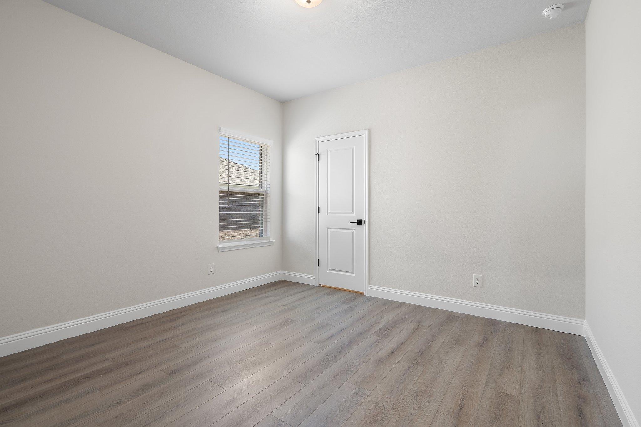 Bright, neutral-toned bedroom in The Holly F floor plan featuring modern wood-style flooring and a single interior door.