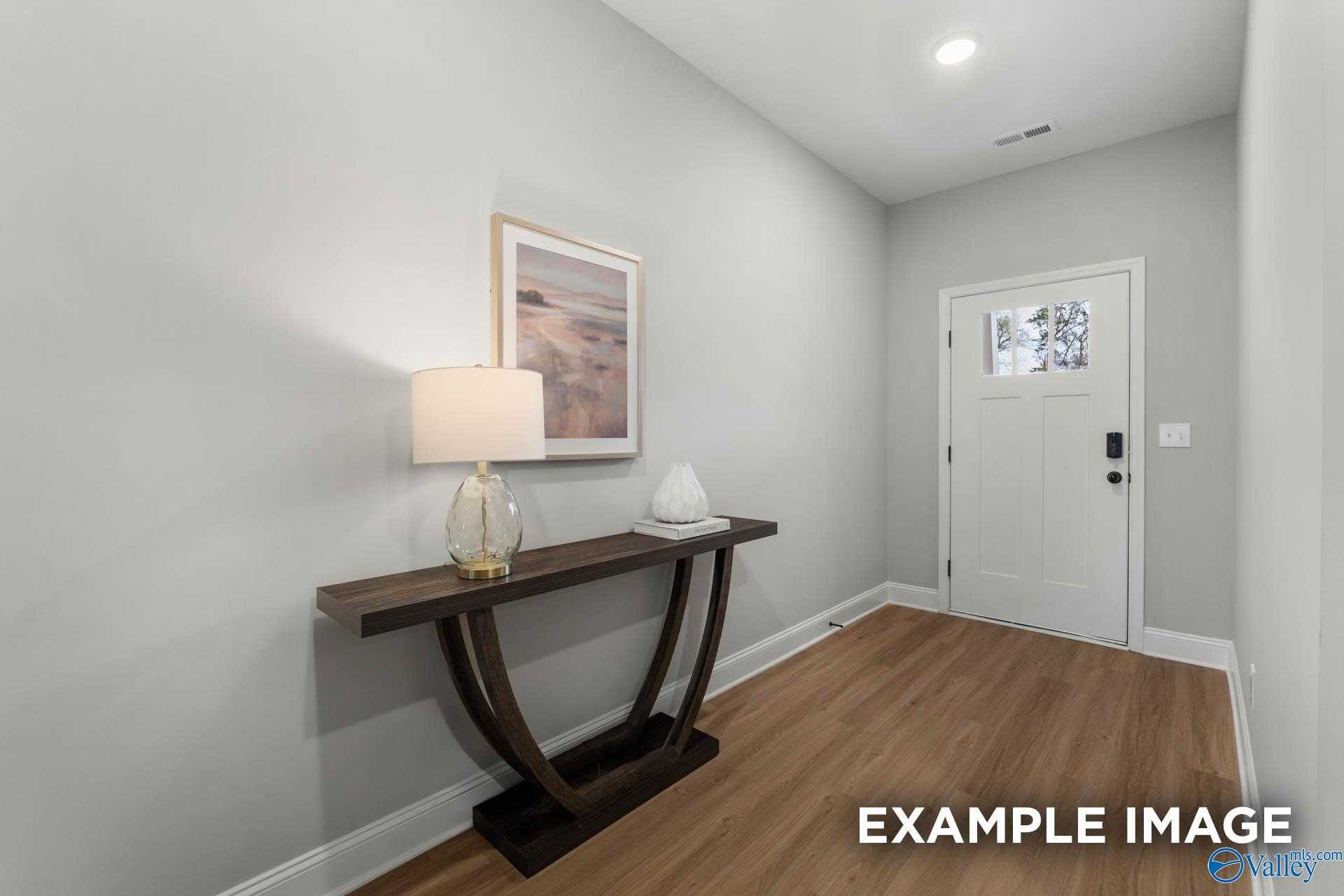 Elegant hallway with light gray walls, dark wood console table, white lamp, and abstract seascape art in Davidson Homes The Daphne C, Owens Cross Roads, AL
