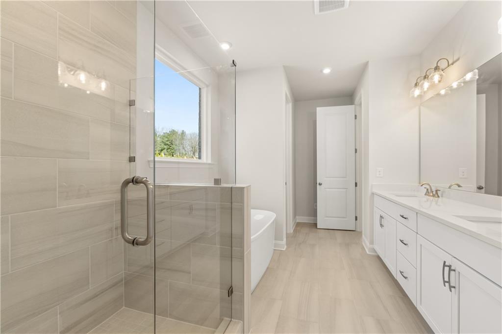 Elegant master bathroom with frameless glass shower, freestanding tub, and double vanity in The Danbury C, Buford, GA