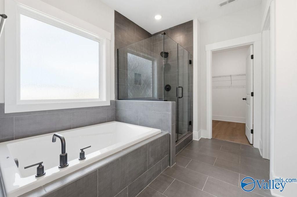 Modern master bathroom featuring freestanding soaking tub, frameless glass shower, and large window in Davidson Homes The Rockford, Hartselle, Alabama