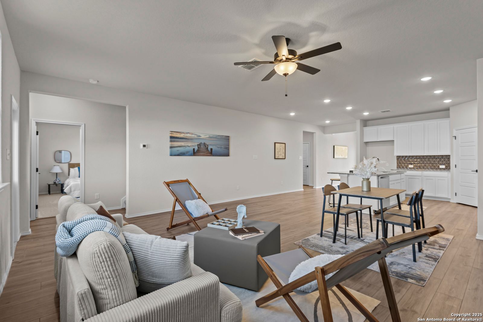 Open-concept living room with beige sofa, lounge chairs, dining table, and white kitchen cabinets in Davidson Homes The Douglas C, Seguin, Texas