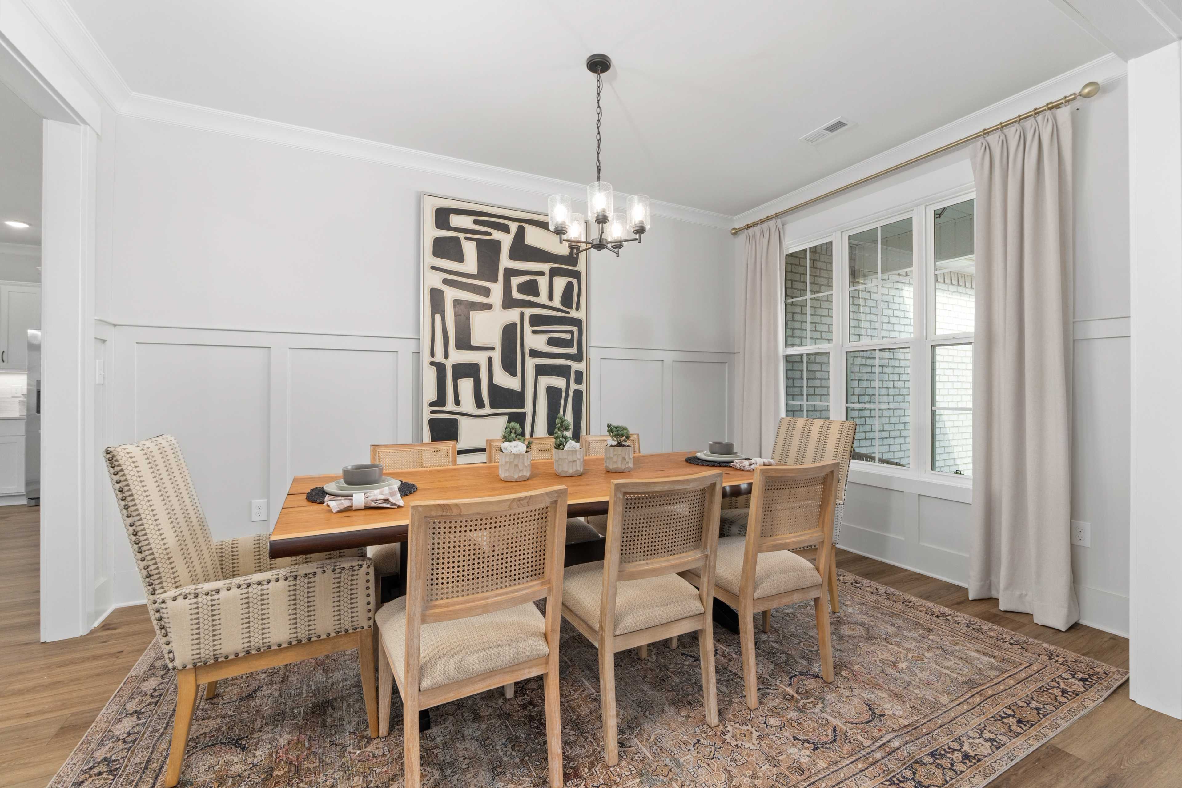 Elegant dining room in Briercreek Meridianville AL by Davidson Homes featuring wooden table, rattan chairs, abstract art, and chandelier