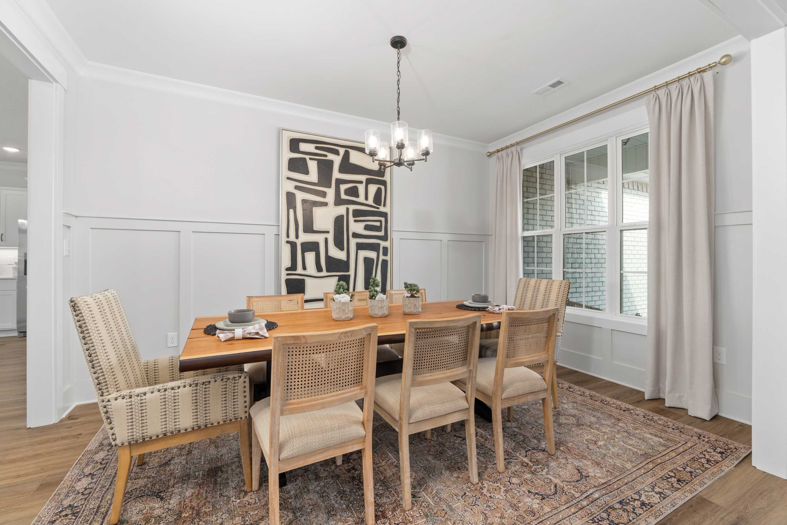 Elegant dining room in Briercreek Meridianville AL by Davidson Homes featuring wooden table, rattan chairs, abstract art, and chandelier