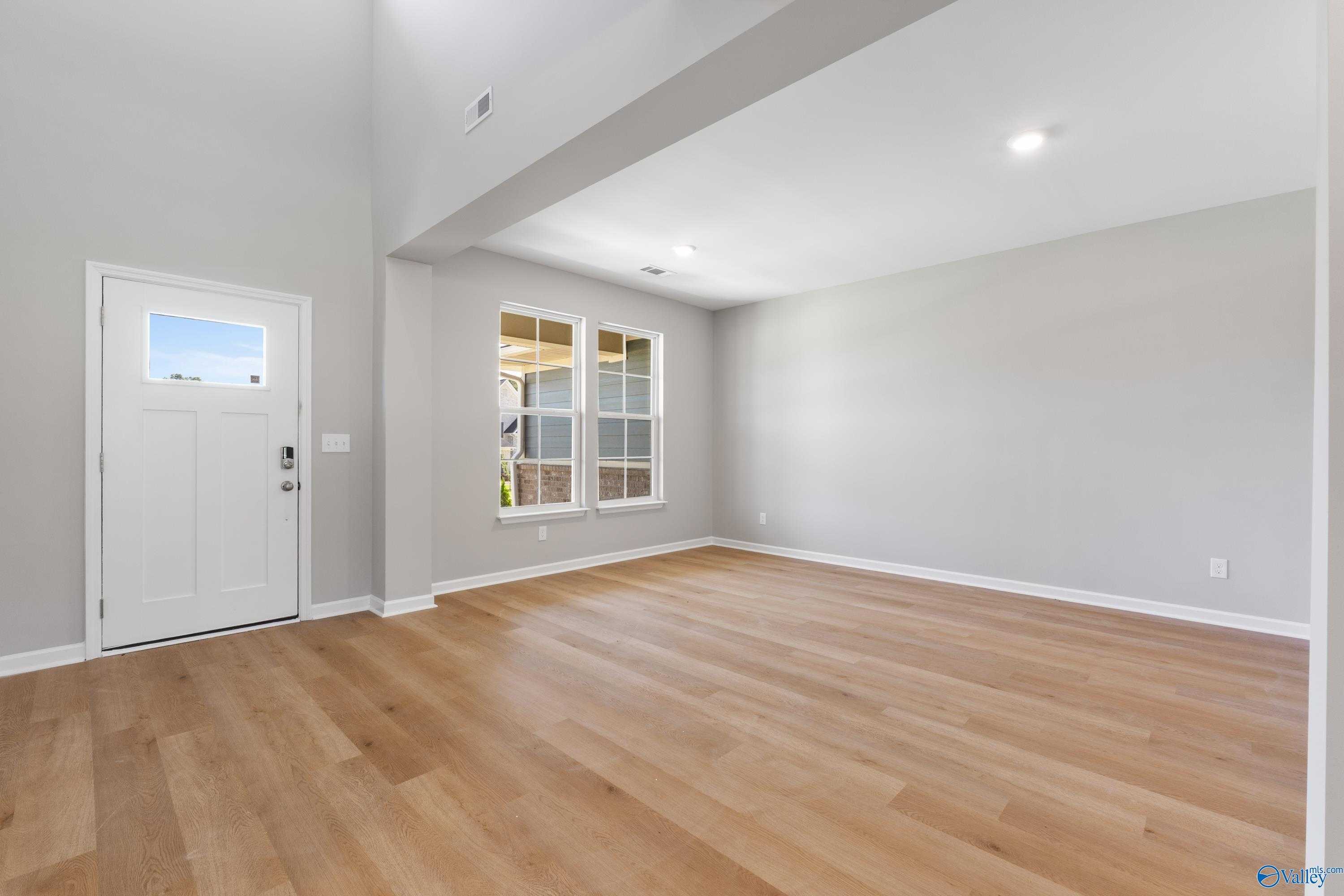 Spacious entry foyer with vaulted ceiling, large grid windows, white door, and oak hardwood floors in Davidson Homes The Charm, Huntsville AL