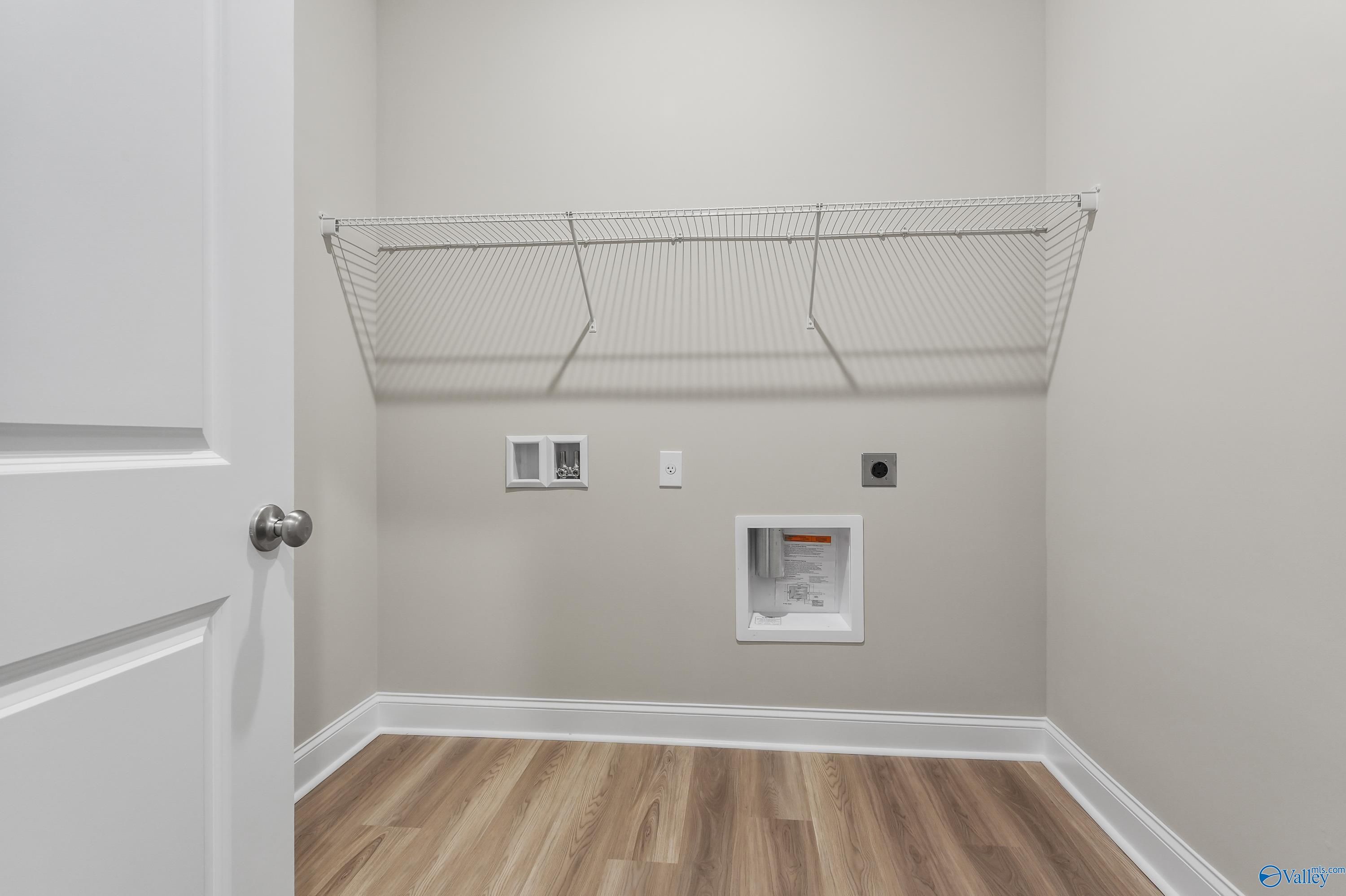 Modern laundry room with wire shelving, utility sink, outlets, and hardwood floors in Evermore Homes The Haven, Owens Cross Roads, Alabama