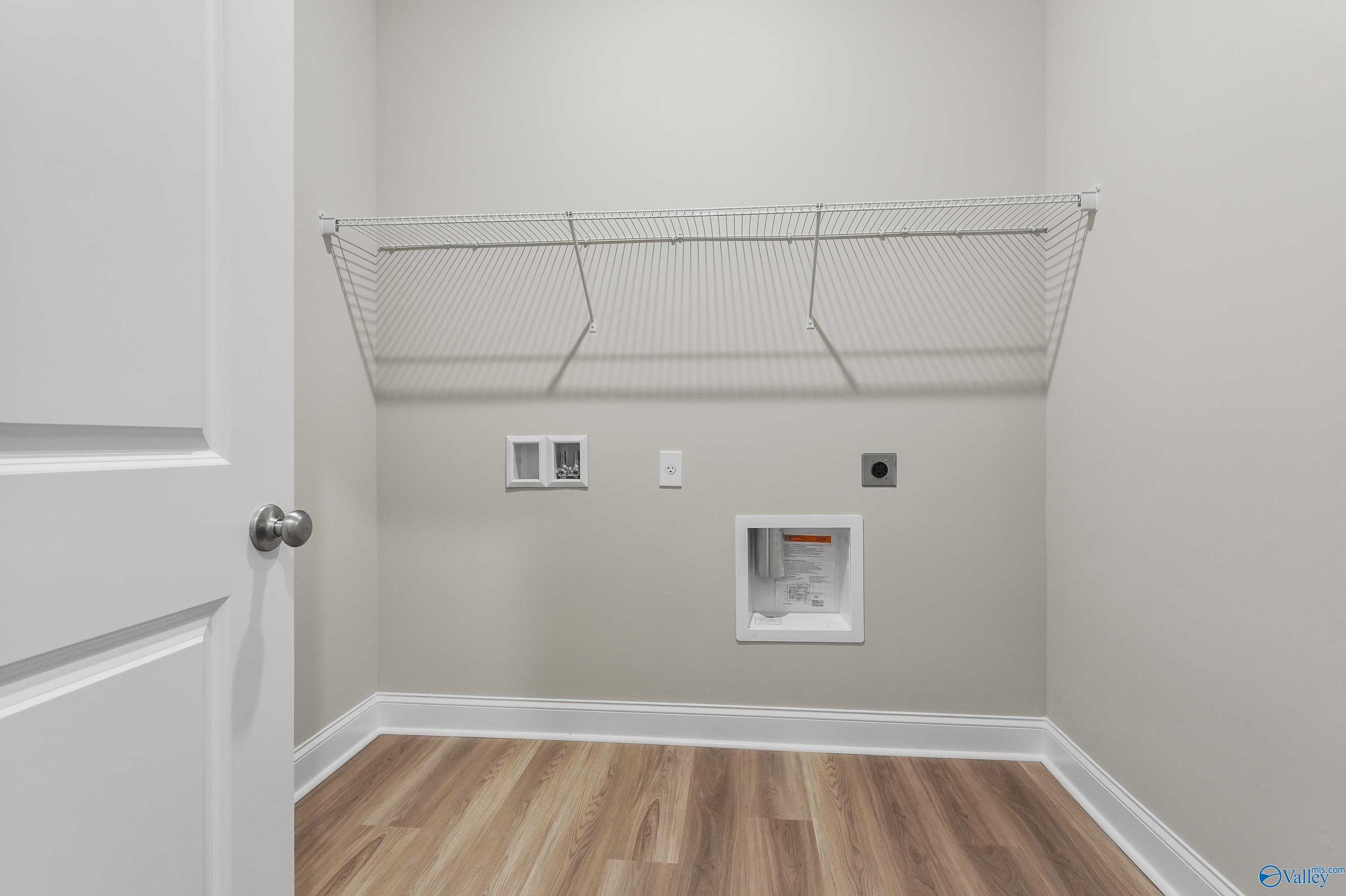 Modern laundry room with wire shelving, utility sink, outlets, and hardwood floors in Evermore Homes The Haven, Owens Cross Roads, Alabama