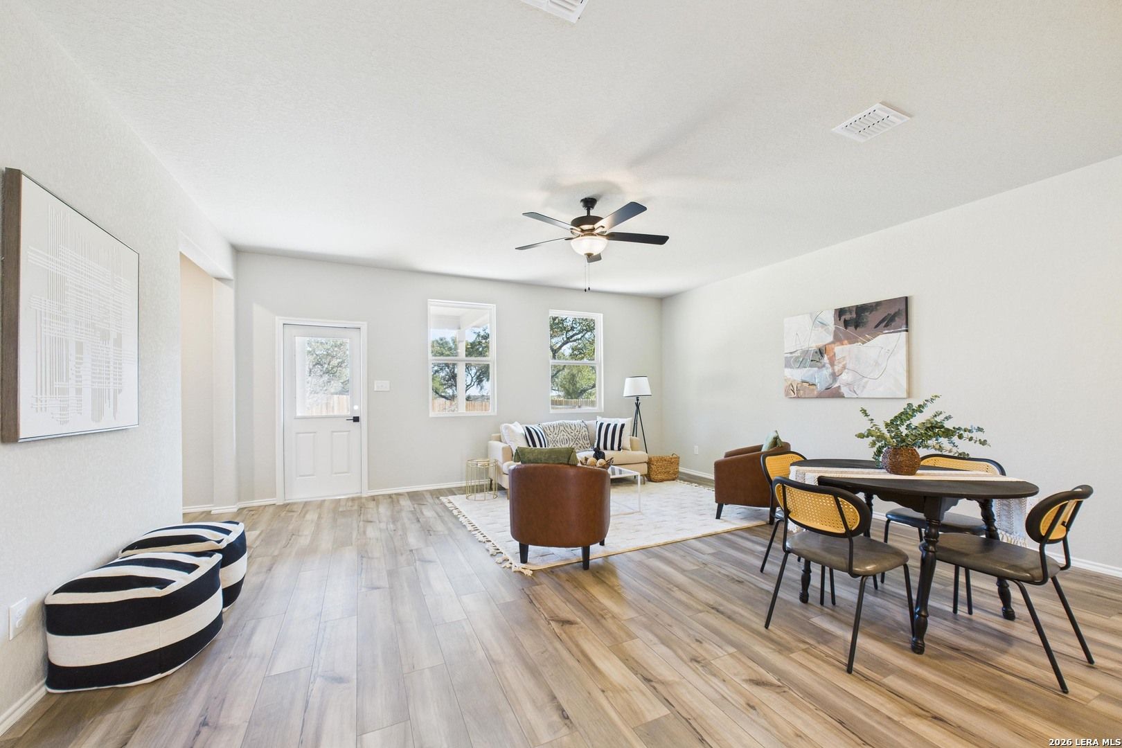 Open living and dining area with hardwood floors, leather sofa, round table, and ceiling fan in Davidson Homes The Douglas E, Bricewood, San Antonio