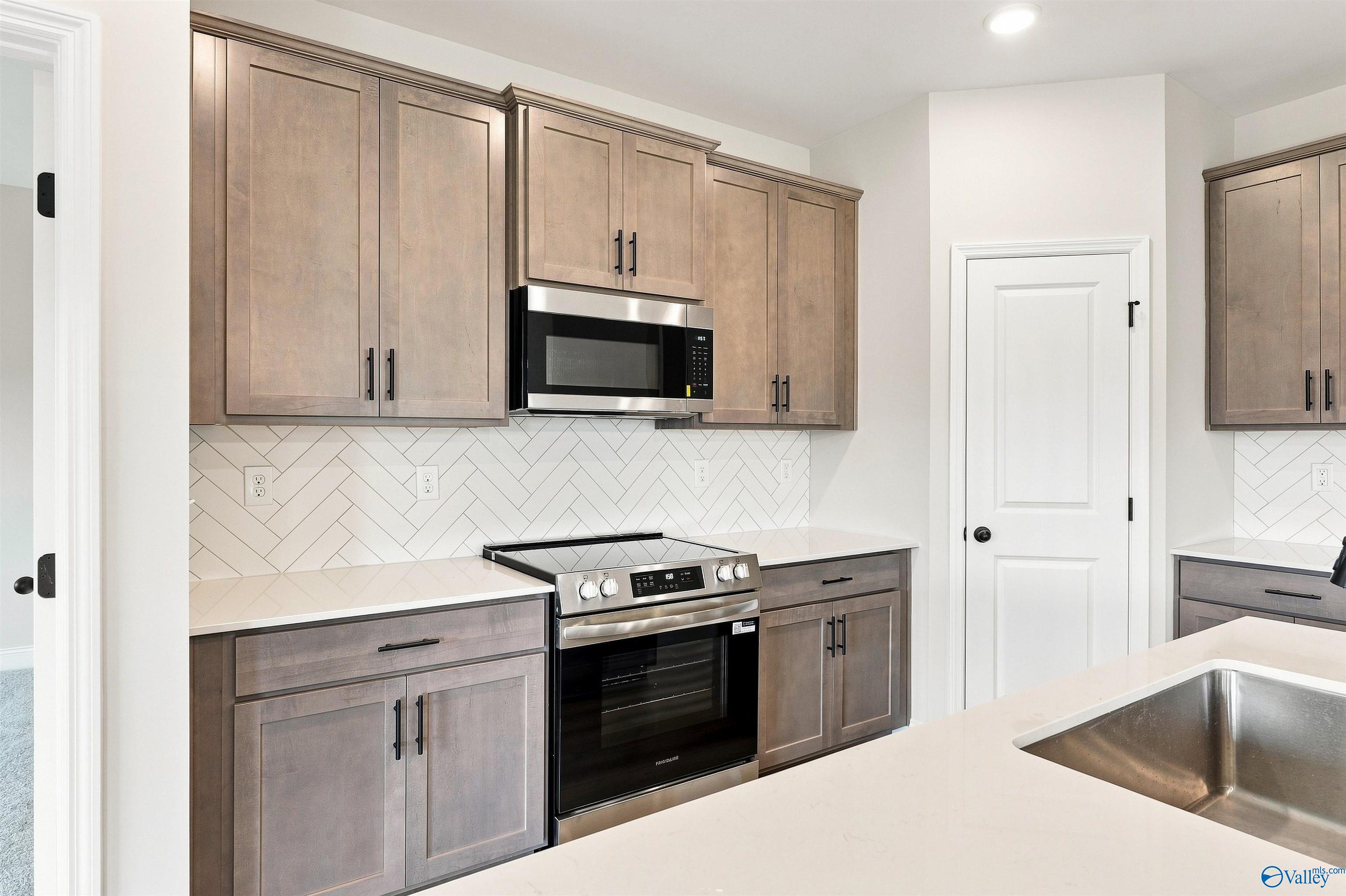 Modern kitchen with stainless appliances, herringbone backsplash, and white countertops in Davidson Homes Franklin C plan, Athens, AL