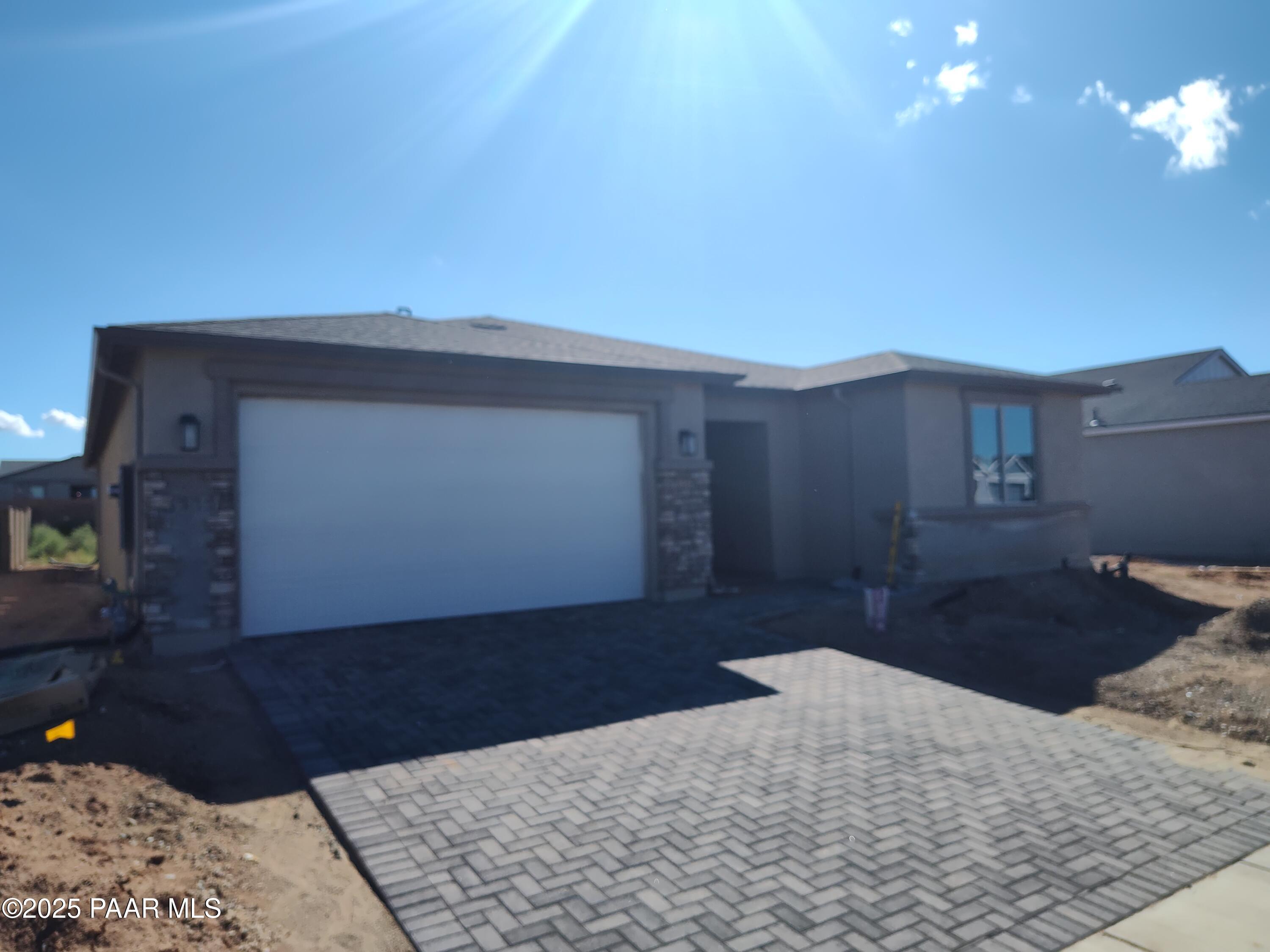 Modern 1-story tan stucco home with 3-car garage, paver driveway, and stone accents in North Ridge at Pronghorn Ranch, Prescott Valley, Arizona