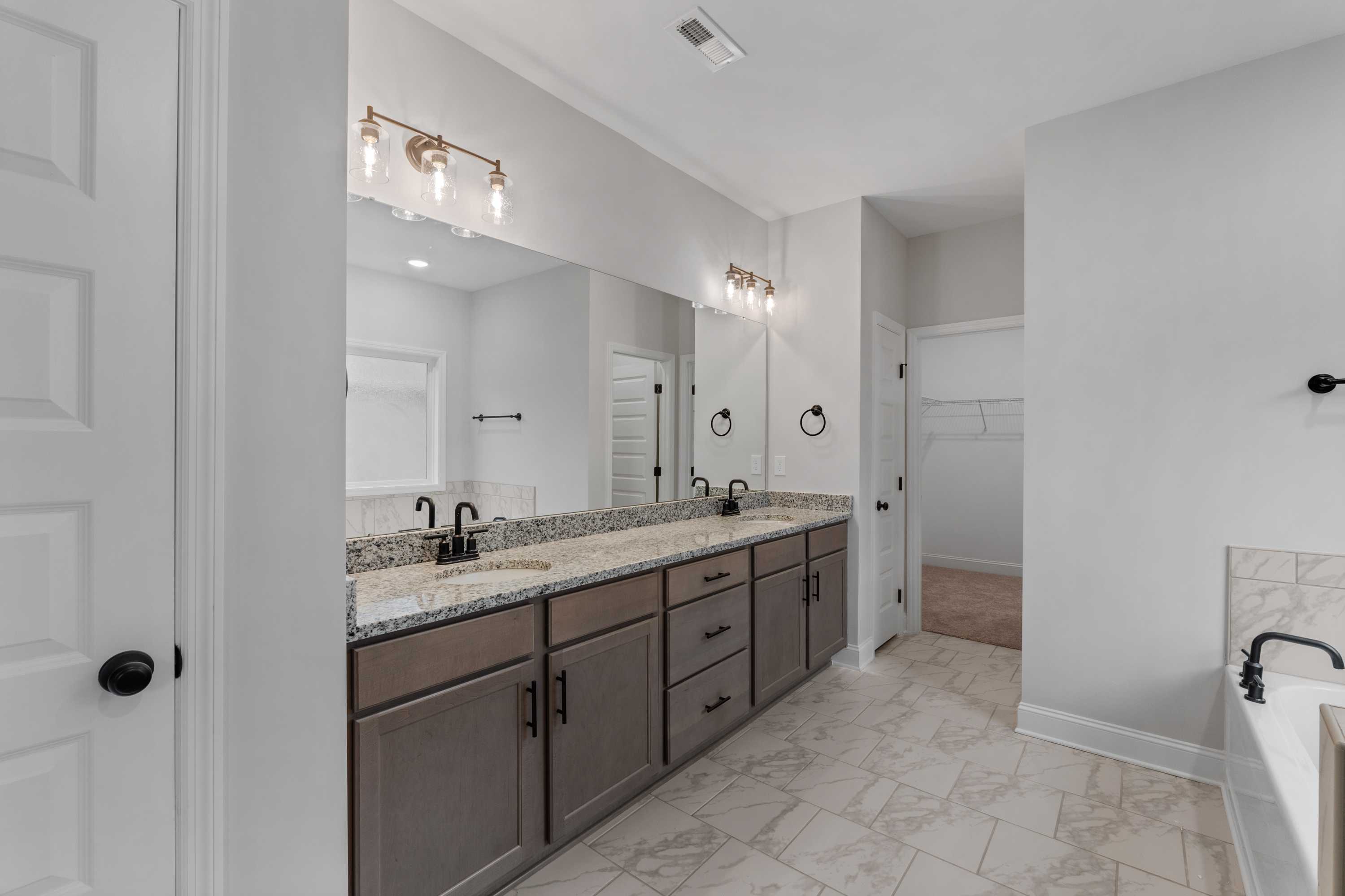 Spacious master bathroom in The Oxford with double vanity, quartz counters, soaking tub, and walk-in closet access