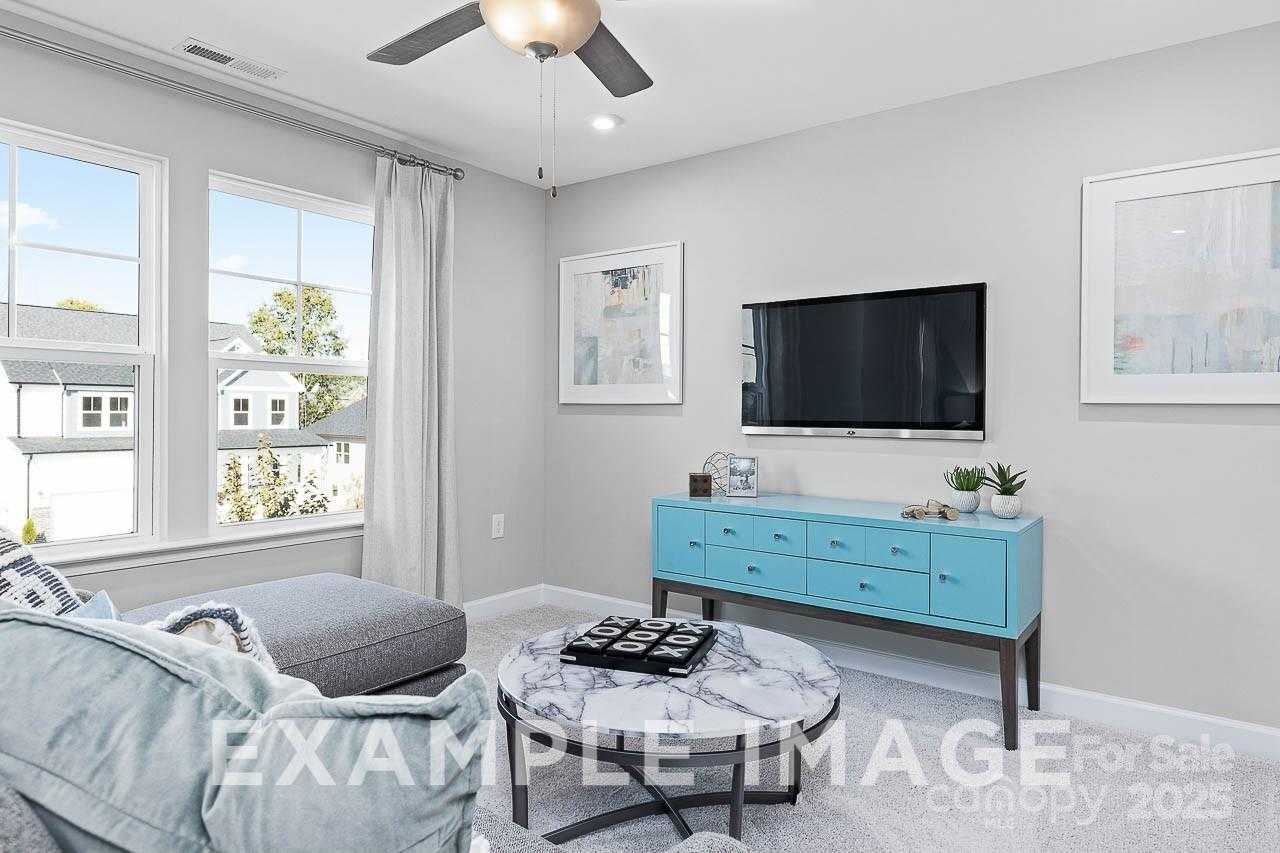 Cozy living room with gray sectional sofa, marble coffee table, blue credenza, mounted TV in The Hemlock A by Davidson Homes, Belmont, NC