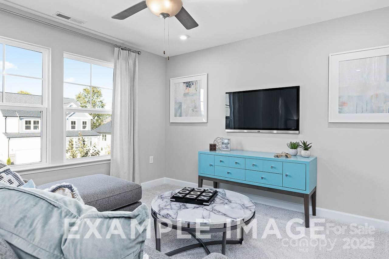 Cozy living room with gray sectional sofa, marble coffee table, blue media console, wall TV, large windows in Davidson Homes The Hemlock A, Belmont, NC